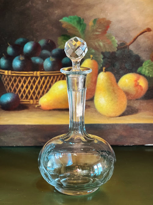 Clear glass decanter with a decorative stopper on a table with fruit in the background
