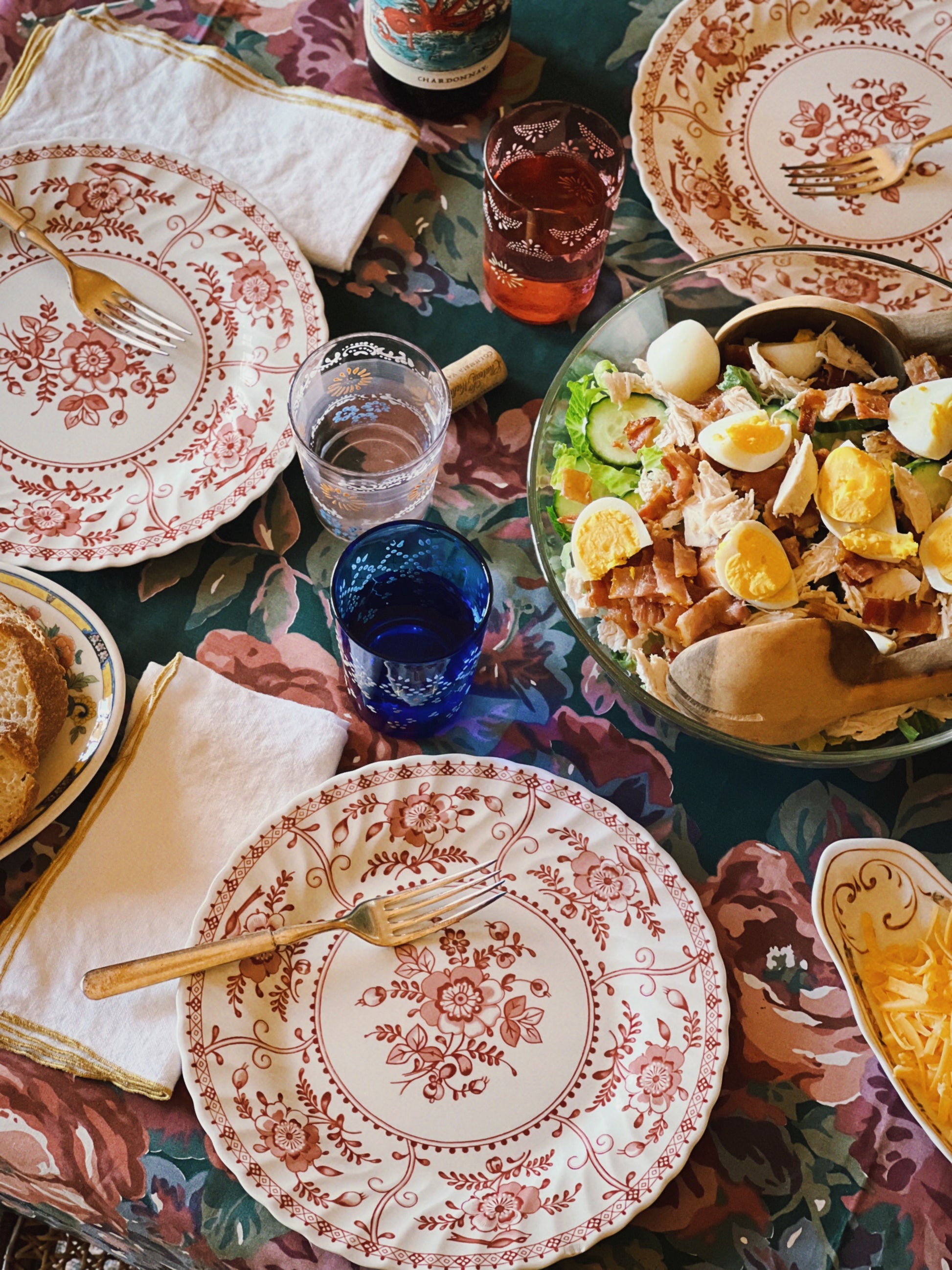 Dining table setting with vintage plates, glasses, and a salad dish.