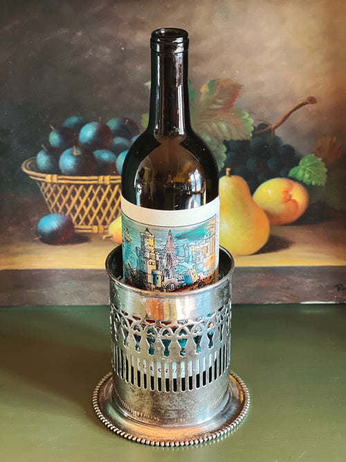 Wine bottle in a decorative holder with a painting of fruits in the background