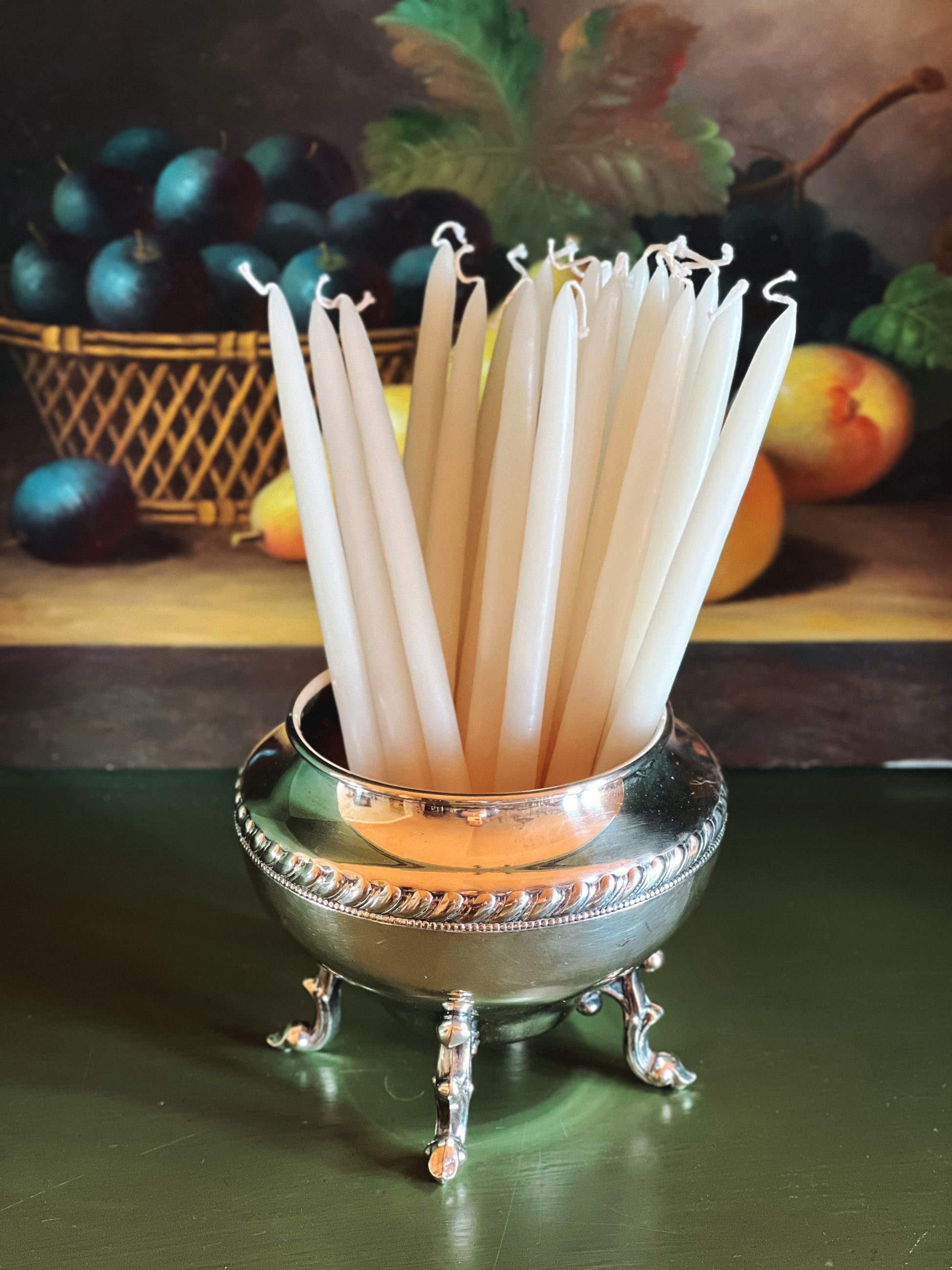 Silver holder with white sticks on a green surface with fruit in the background