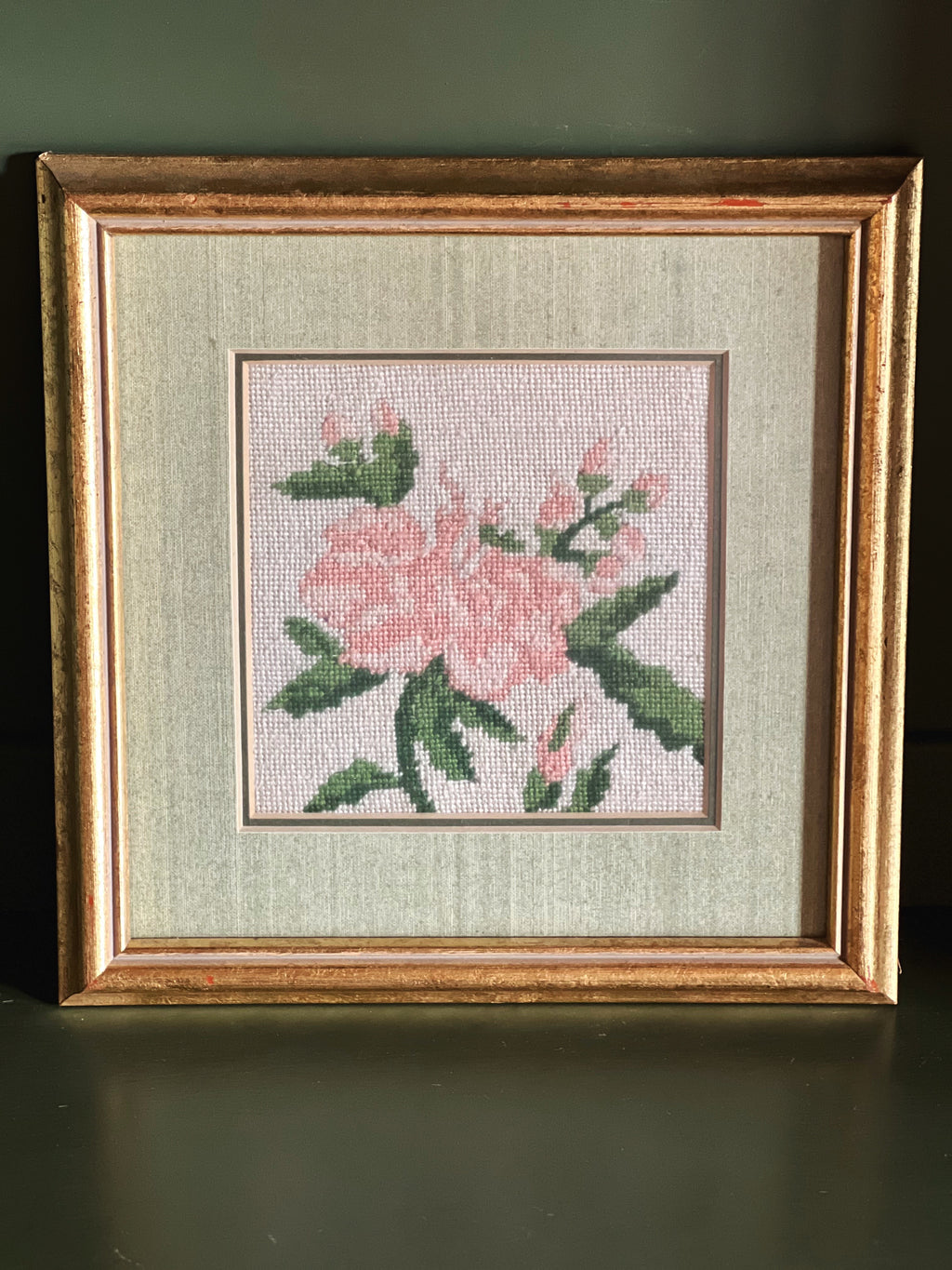 Framed cross-stitched floral design on fabric with a gold frame.