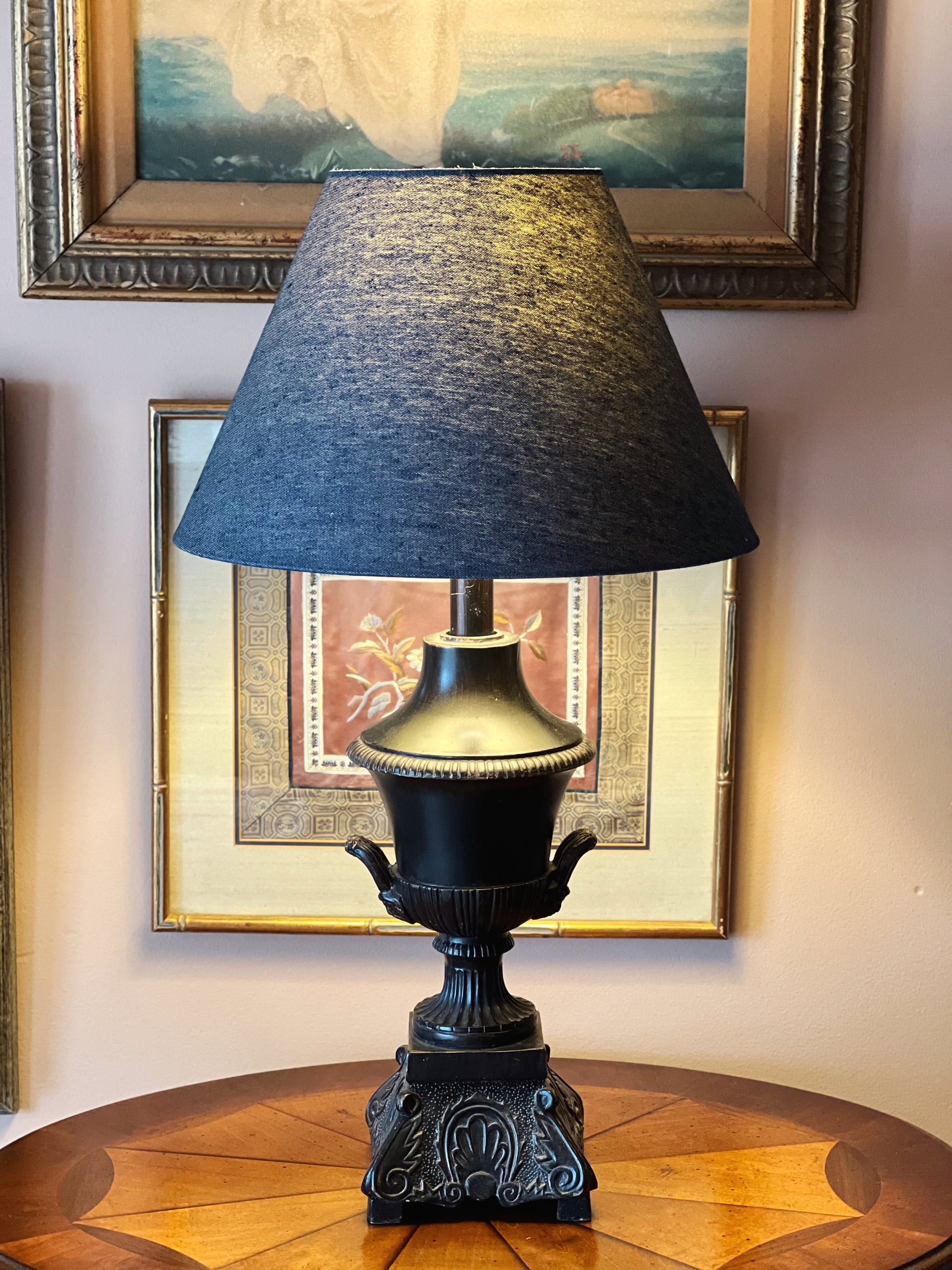 Decorative lamp with a black shade on a wooden table against a wall with framed pictures.