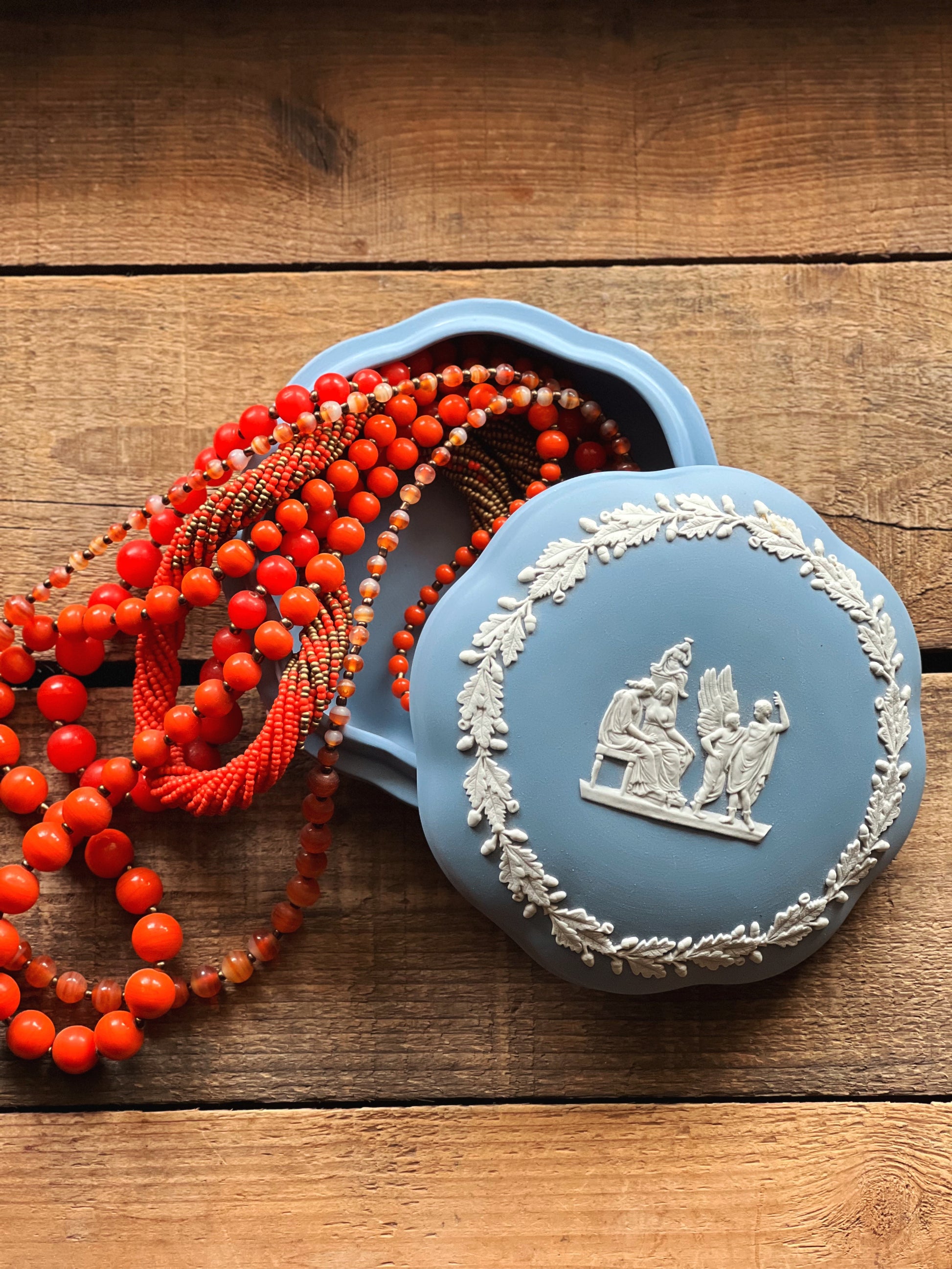 Decorative blue box with intricate design on a wooden surface, accompanied by a red beaded necklace.