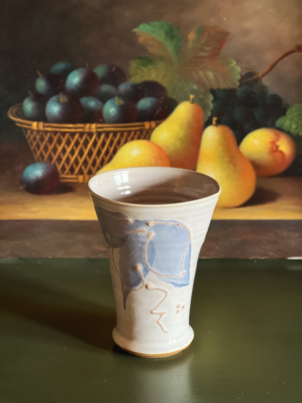 Vase with decorative design on a table with fruits in the background