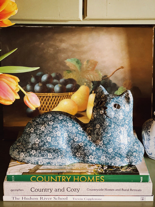 Decorative blue bird figurine on a book titled 'Country Homes' with tulips and a painting in the background.