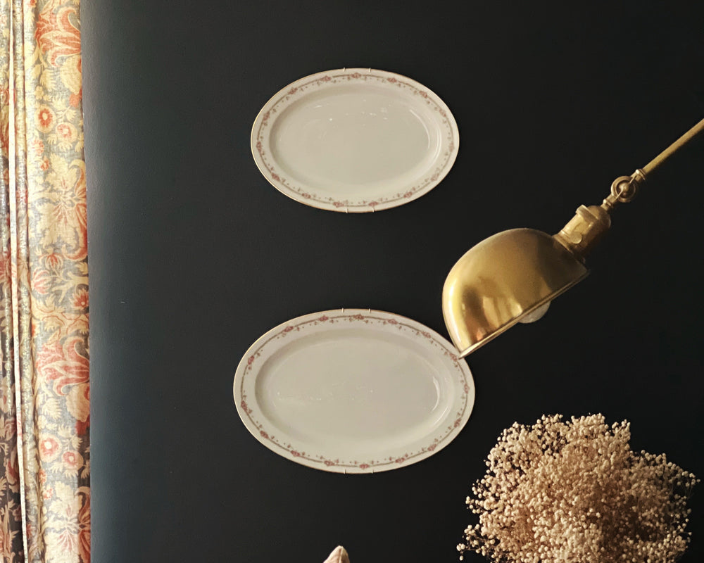 Three oval plates on a dark wall with a gold spoon and decorative elements.