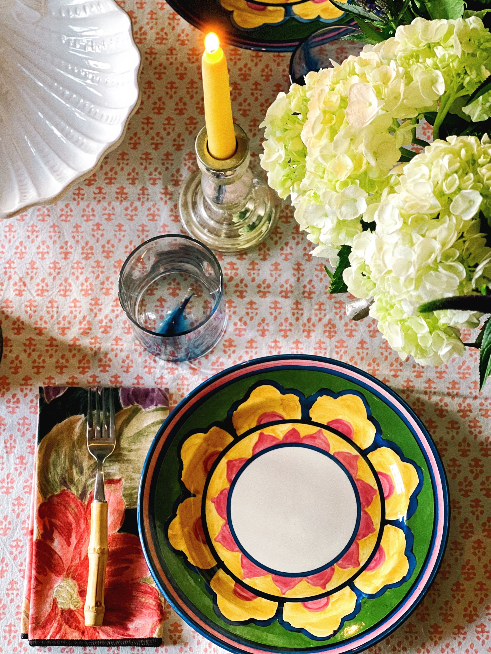 Set of four hand-painted vintage dinner plates with colorful floral pattern styled on a table with hydrangeas and candlelight
