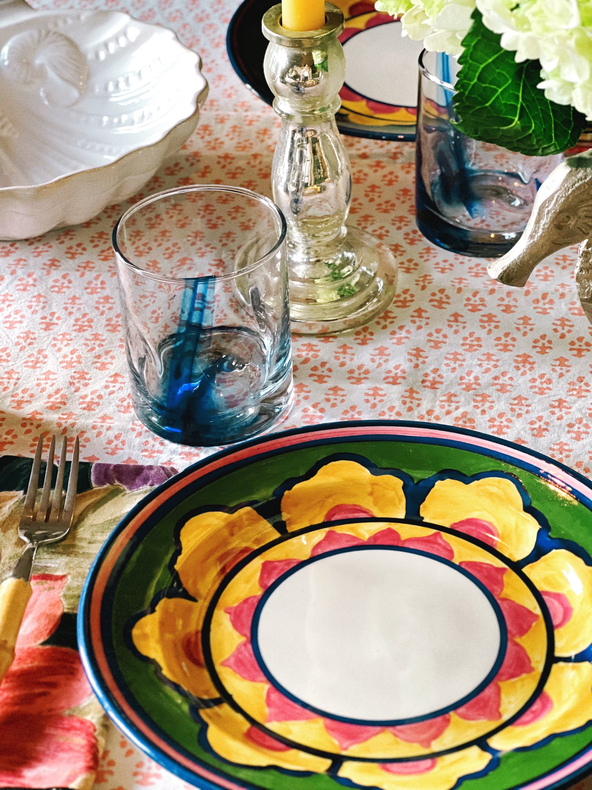 Colorful vintage floral dinner plates layered in a styled table setting with glassware and linen
