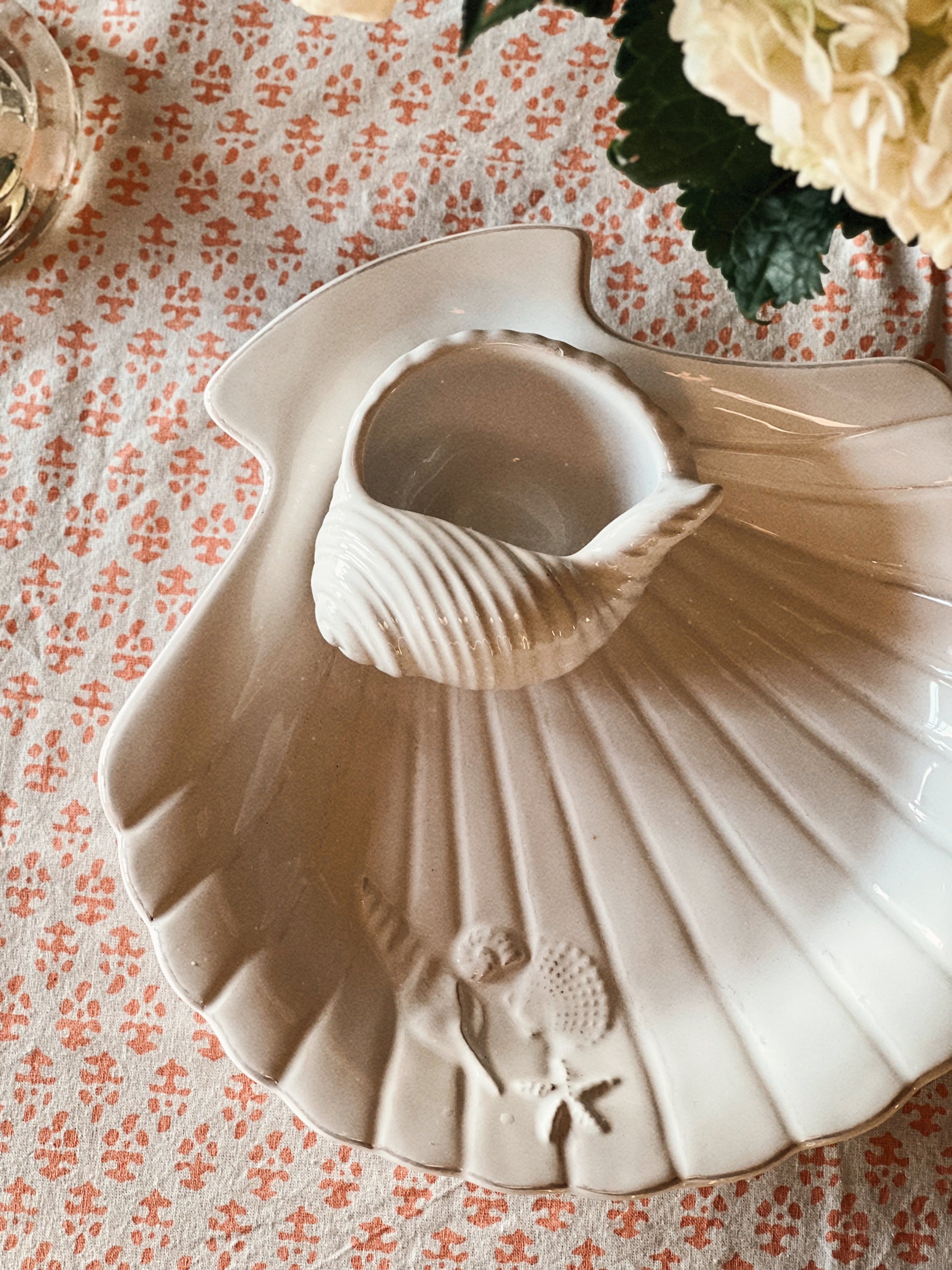 Ceramic scallop shell chip and dip serving dish on a coastal table with hydrangeas