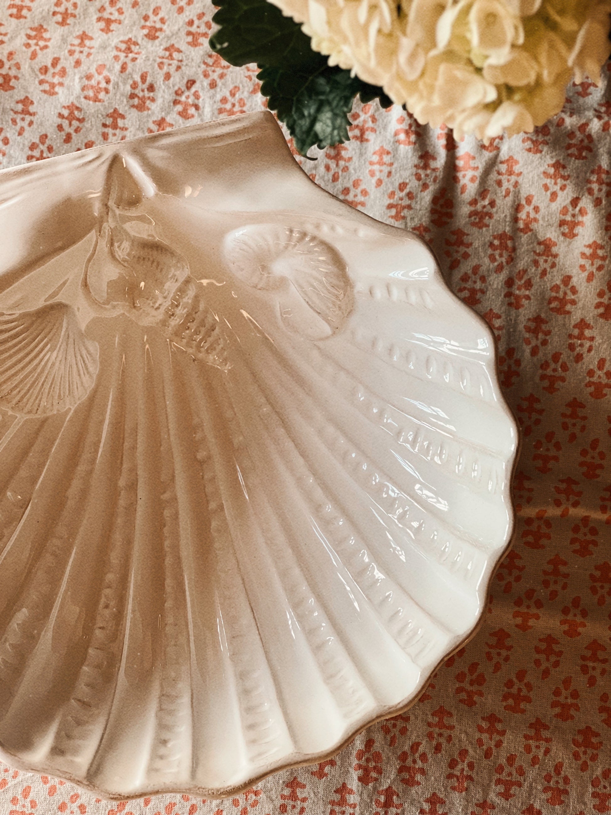White ceramic scallop shell serving dish on a coastal-inspired table with hydrangeas