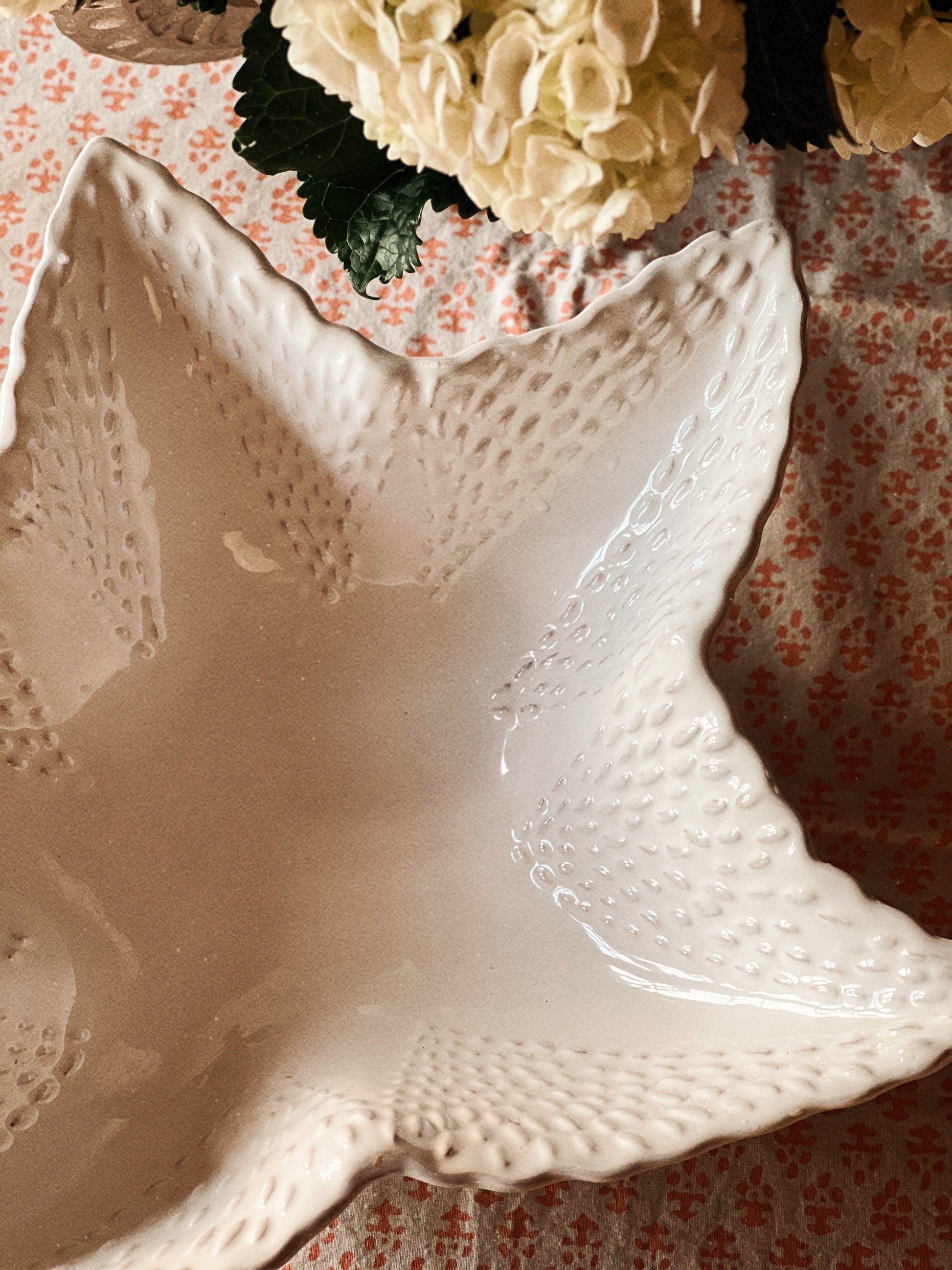 Large ceramic starfish serving bowl with embossed texture styled on a patterned tablecloth with hydrangeas and candlelight