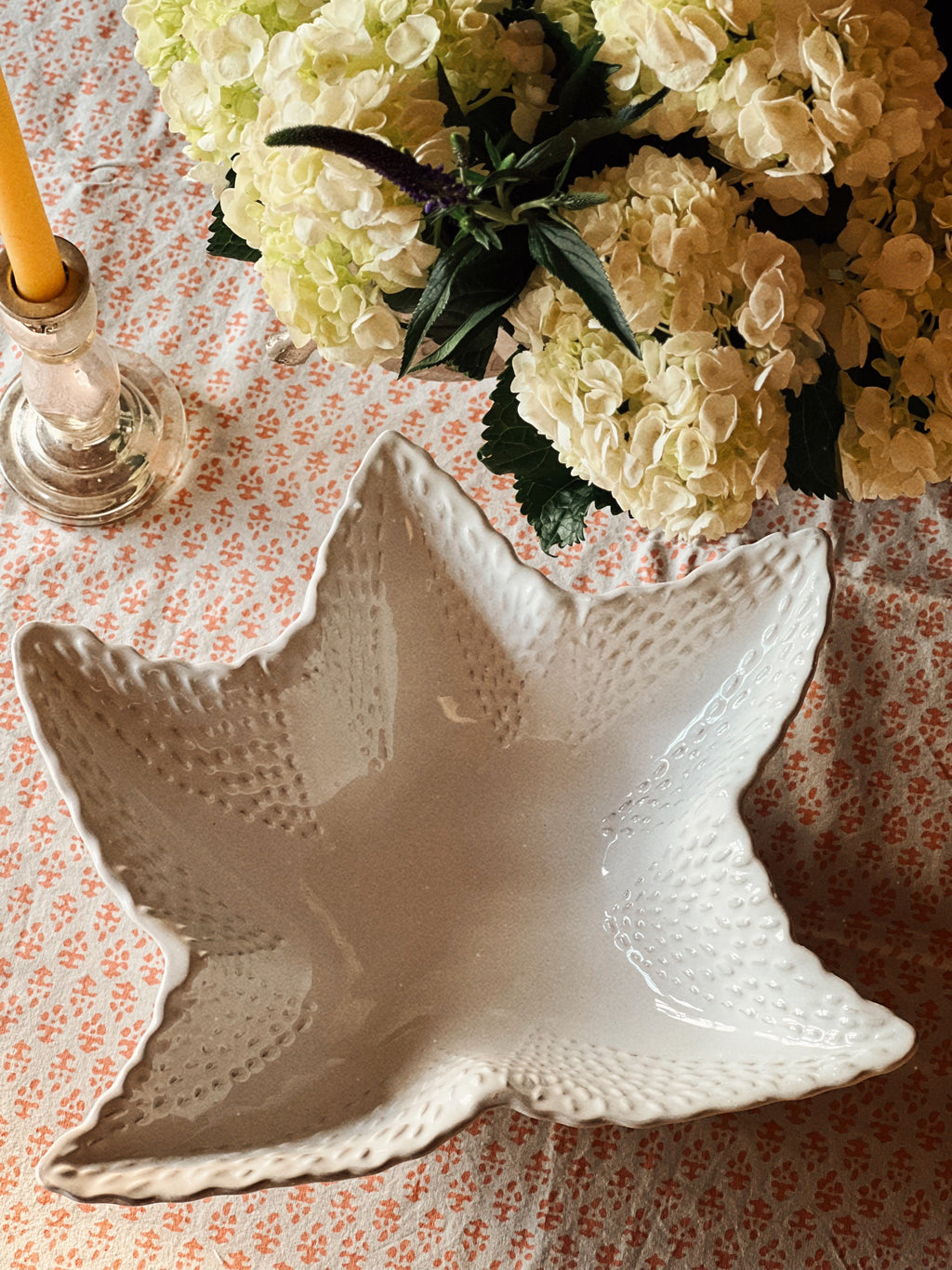 Starfish-shaped ceramic bowl used as a centerpiece filled with white hydrangeas on a styled dining table