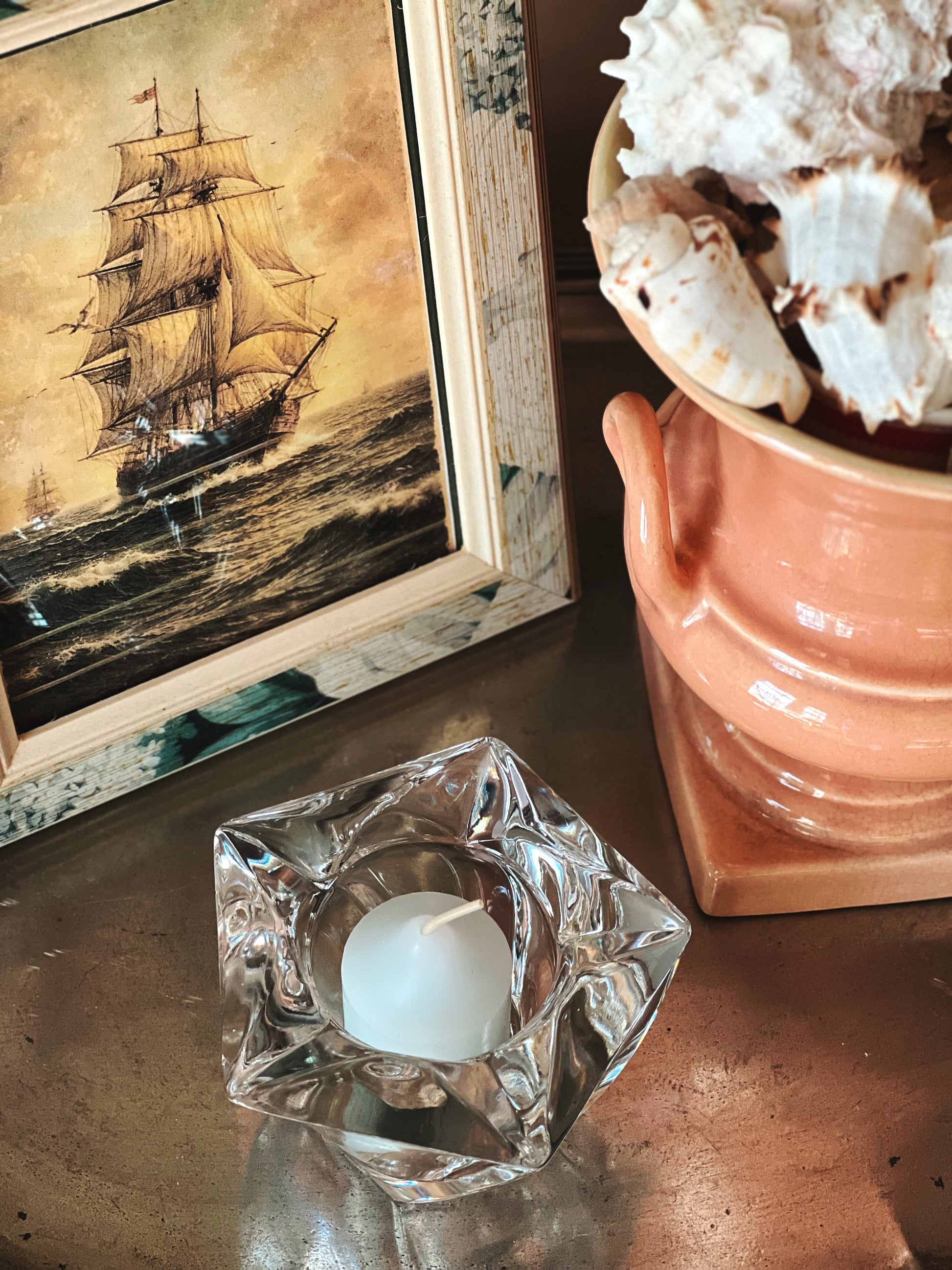 Vintage crystal starfish votive holder styled with coastal artwork and shell decor on wooden surface