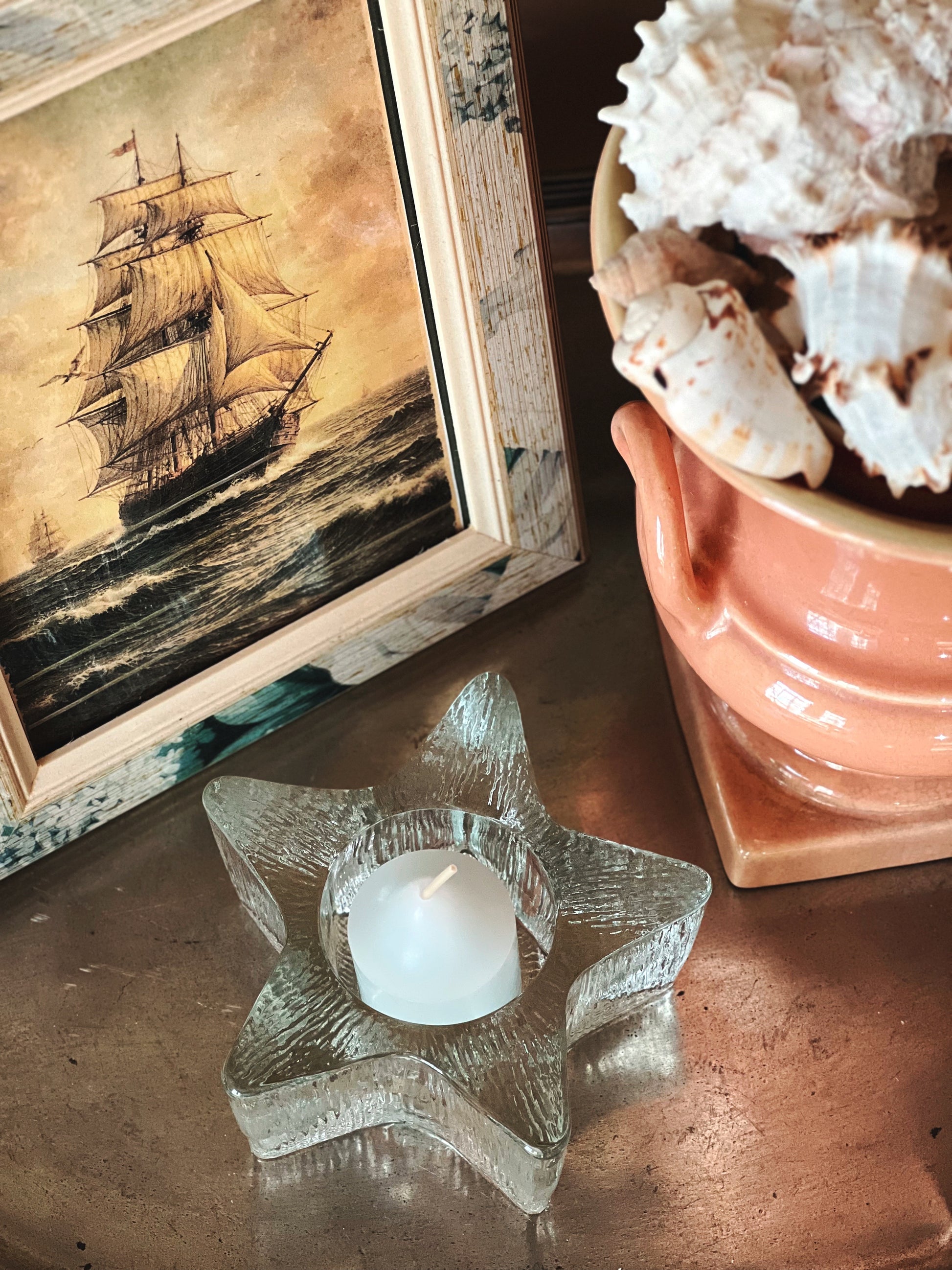 Vintage glass starfish votive holder styled with coastal artwork and shell decor on metal surface