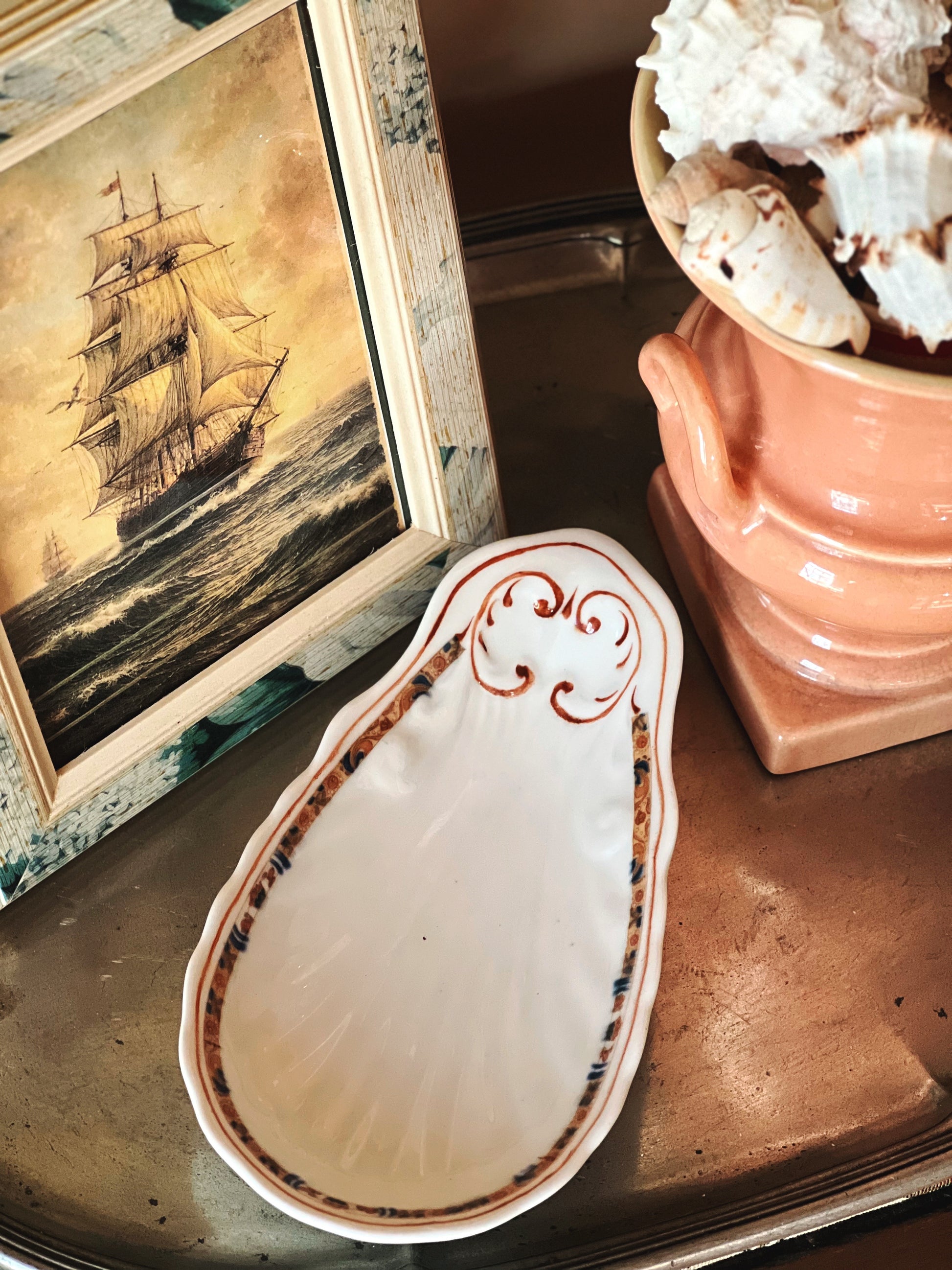 Vintage shell shaped relish dish styled with coastal artwork and collected decor on wooden surface