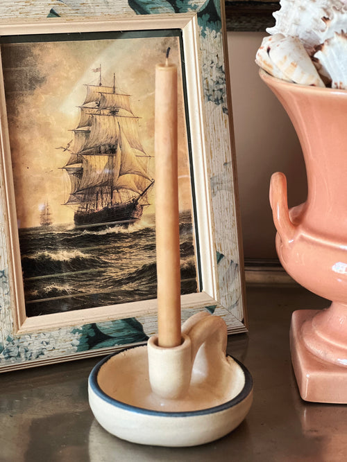 Vintage handmade pottery taper candle holder with blue trim on cream earthenware base, styled with framed nautical artwork and soft neutral decor
