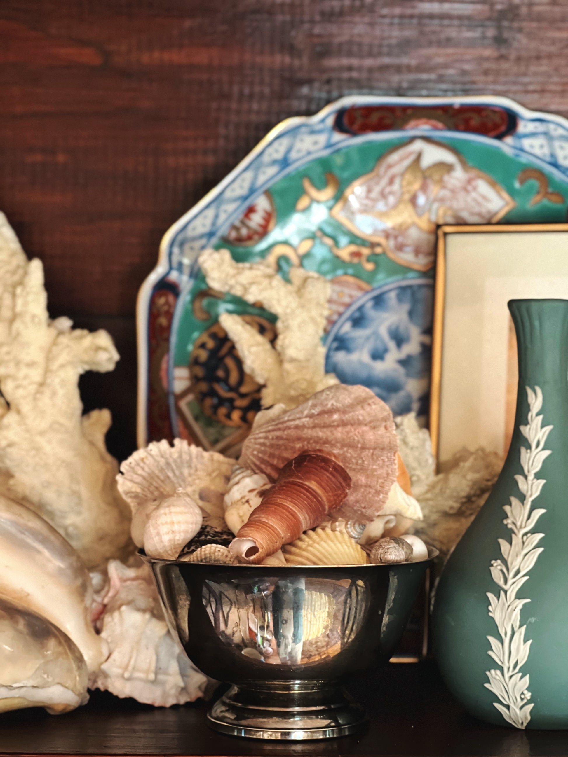 Decorative chinoiserie plate on a shelf with shells and coastal decor