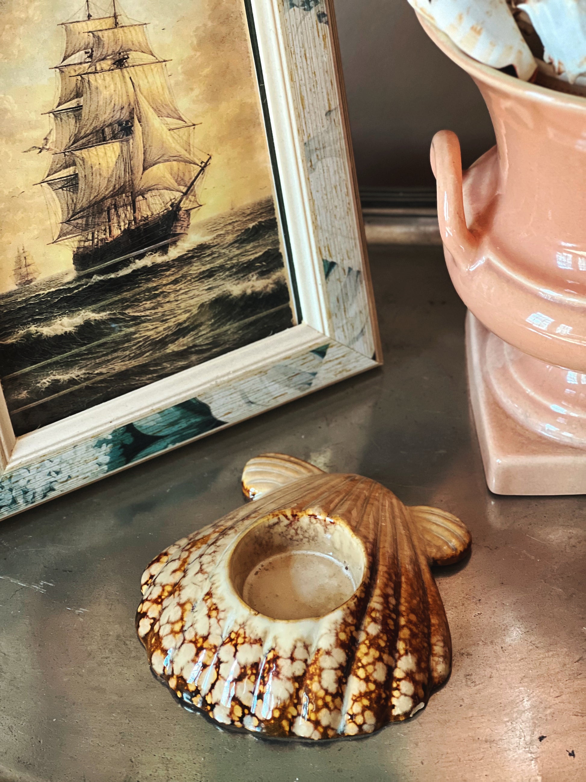 Vintage ceramic seashell votive candle holder in natural brown tones styled beside framed nautical artwork