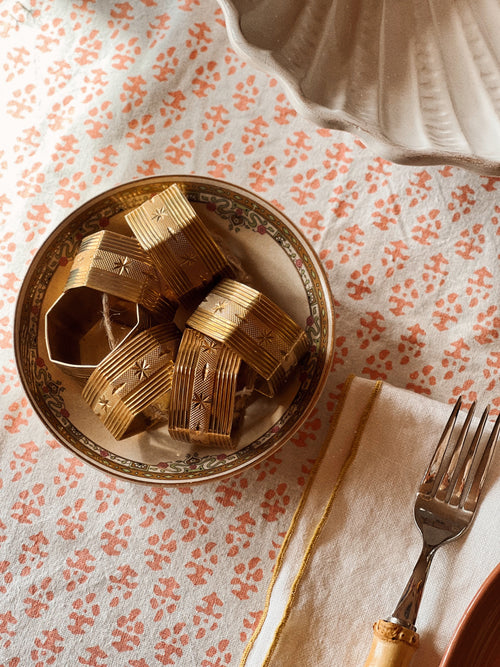 Set of vintage brass napkin rings with starburst design arranged on a patterned tablecloth
