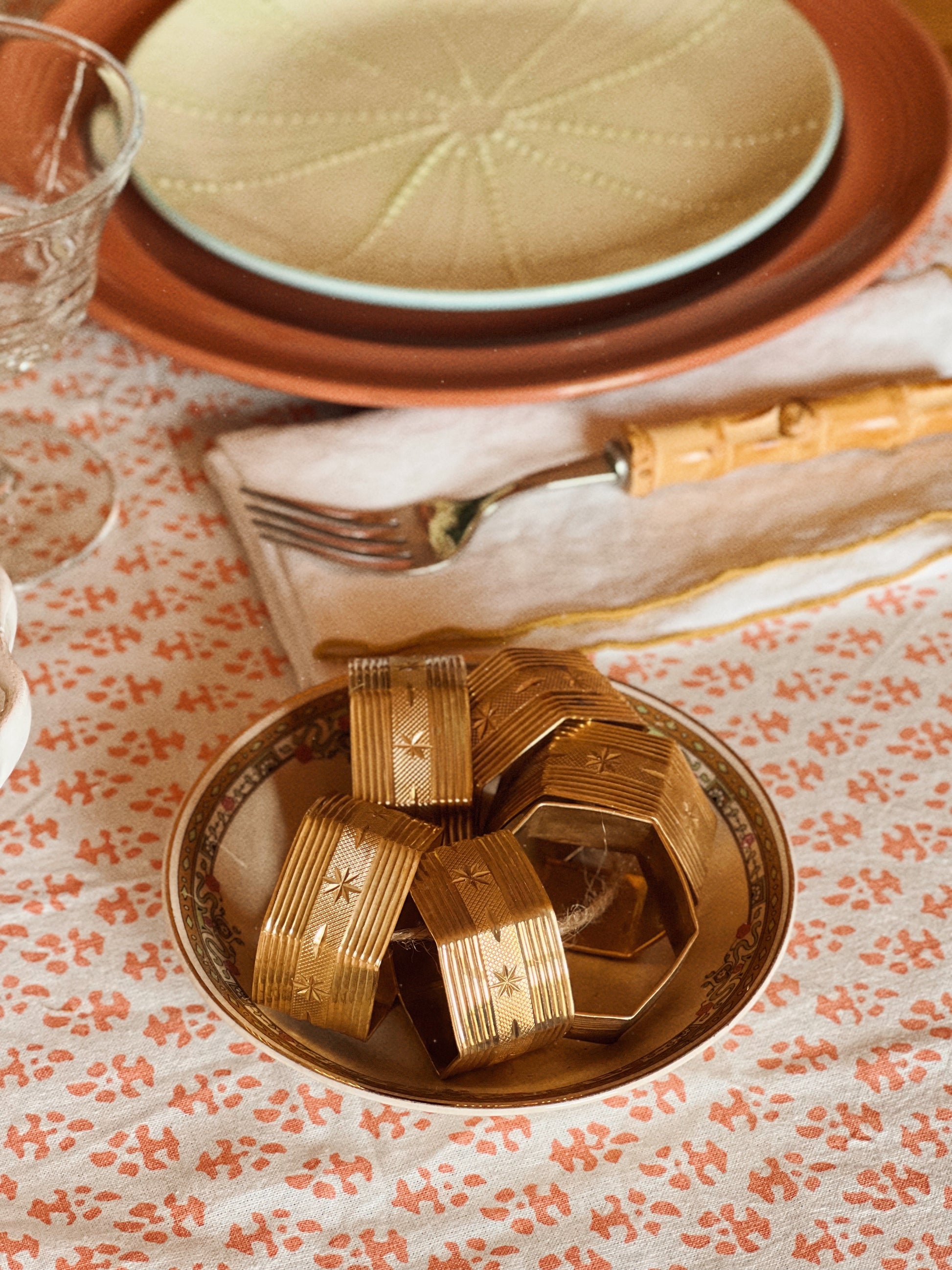 Vintage brass starburst napkin ring holding a folded cloth napkin in a layered table setting
