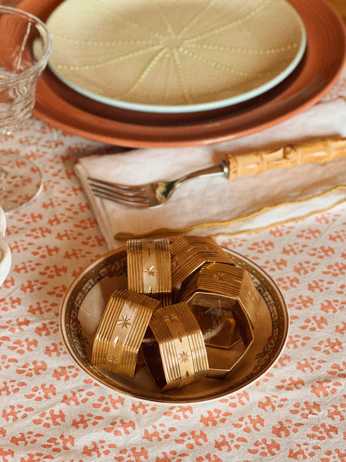 Vintage brass starburst napkin ring holding a folded cloth napkin in a layered table setting
