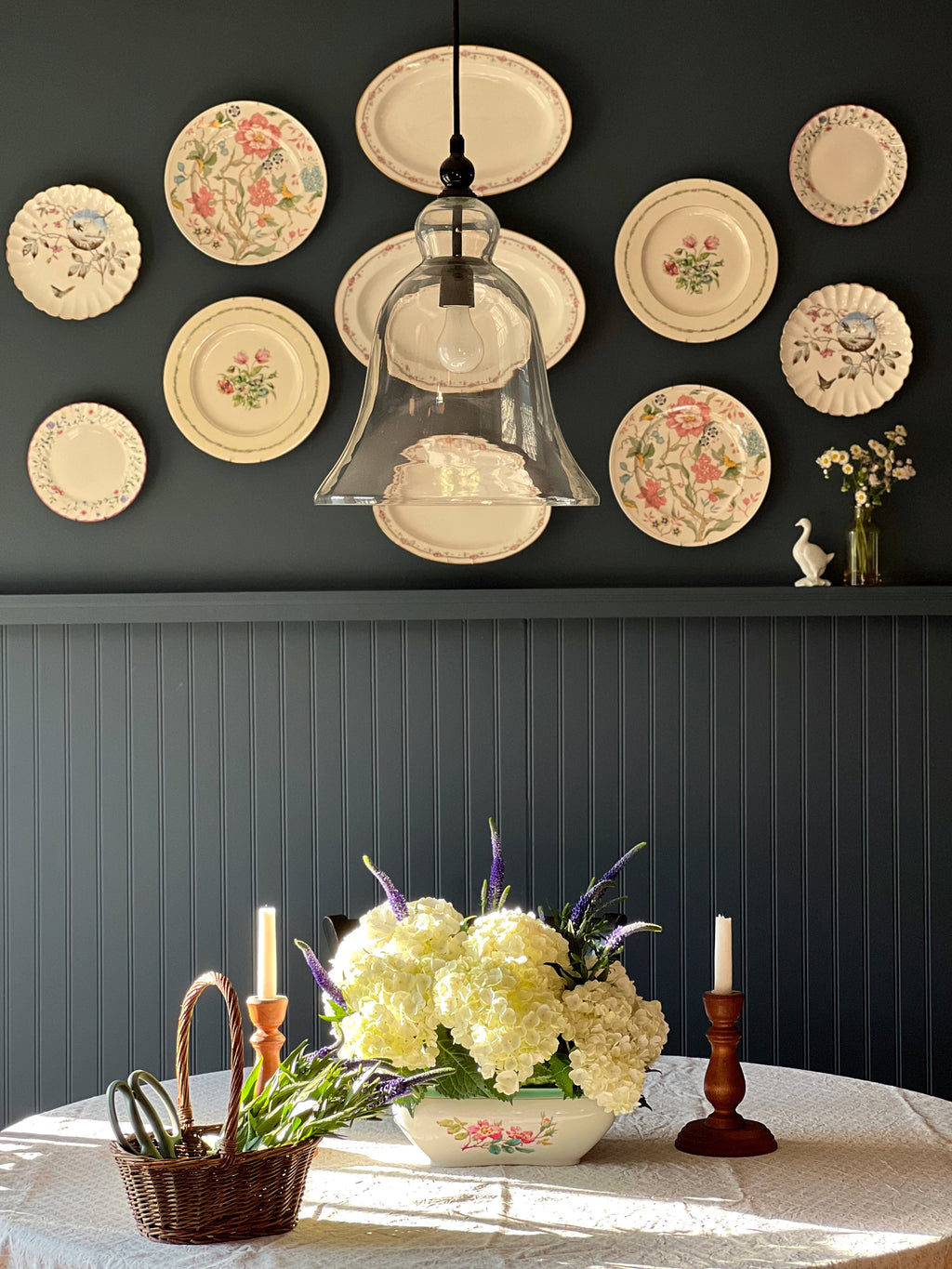 vintage woven basket with greenery on dining table styled beneath plate wall