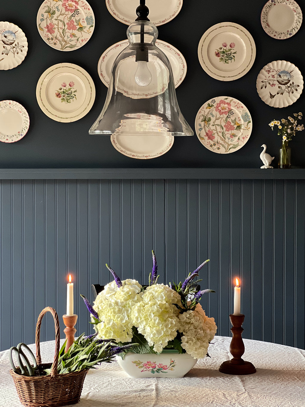Haviland Limoges floral tureen used as centerpiece with hydrangeas on dining table beneath vintage plate wall