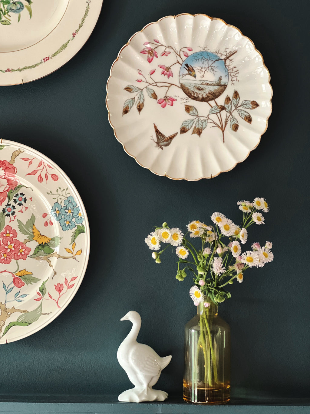 small white goose figurine styled beneath vintage floral plate wall with glass bud vase