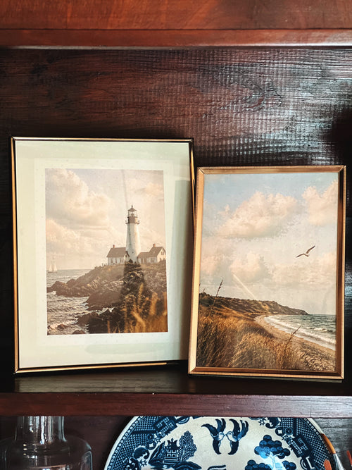 pair of vintage brass picture frames styled on wooden shelf with coastal artwork and layered home decor