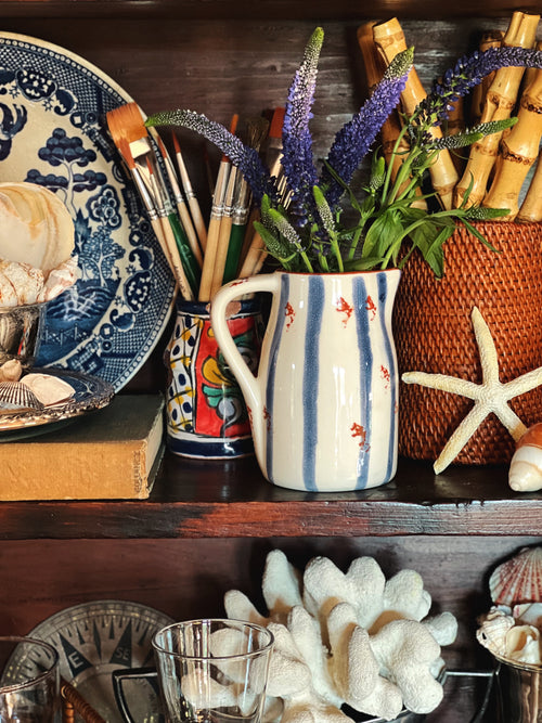 Small coastal ceramic creamer pitcher with blue stripe design, styled on a shelf with vintage decor and florals