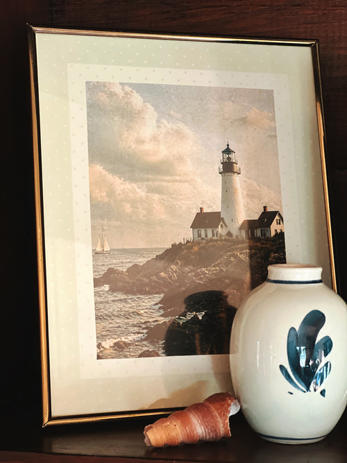 vintage brass frames with lighthouse and coastal landscape artwork displayed in shelf vignette