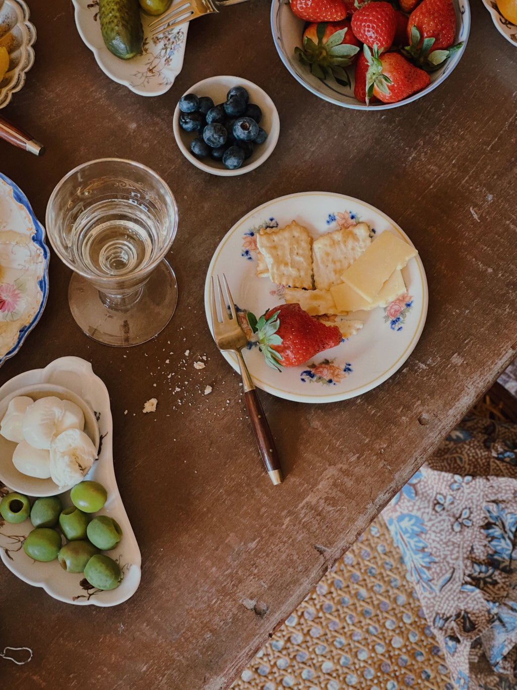 vintage appetizer plates set with strawberries, honeycomb, olives and glassware on rustic wooden table