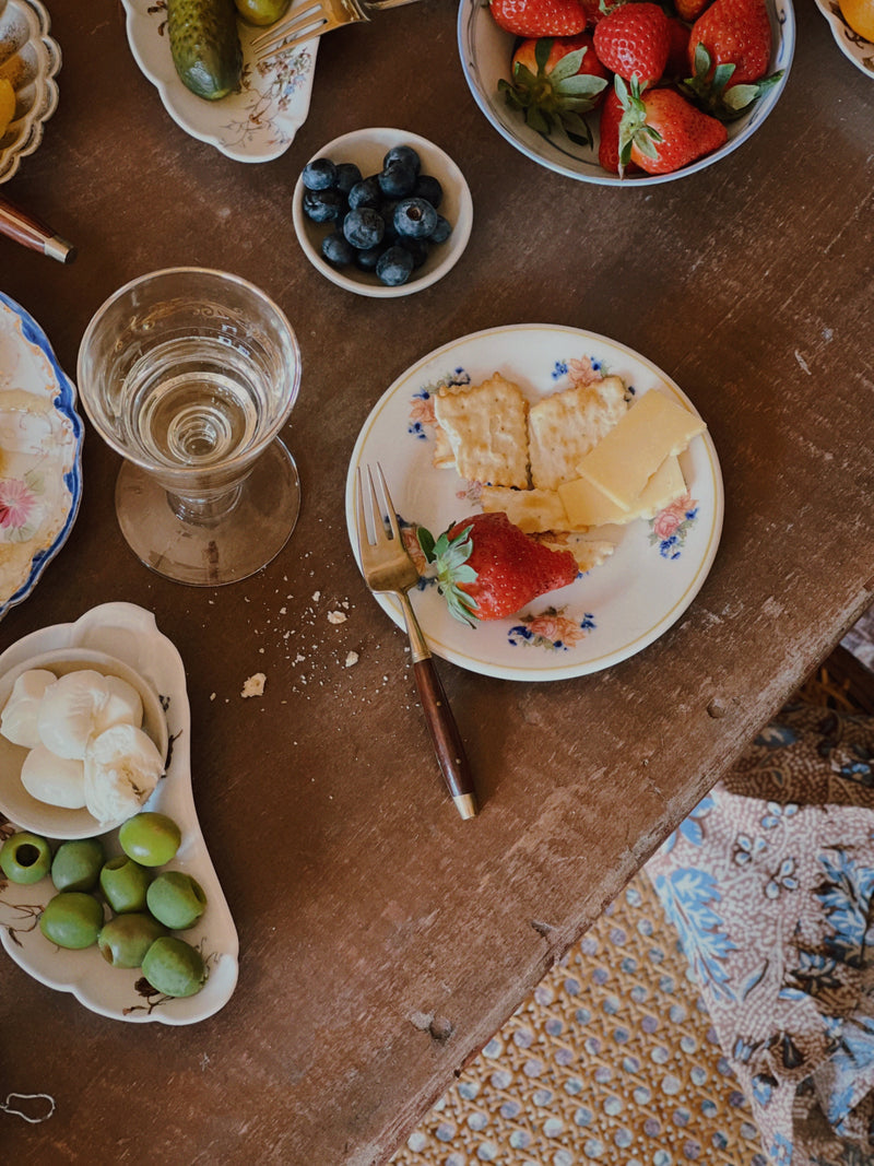 vintage appetizer plates set with strawberries, honeycomb, olives and glassware on rustic wooden table
