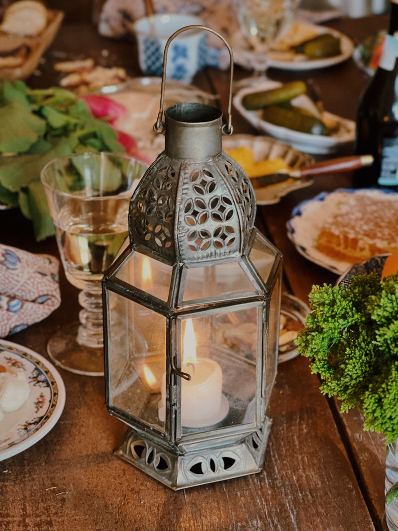 Vintage Moroccan style metal and glass lantern with candle styled on a table with layered vintage tableware