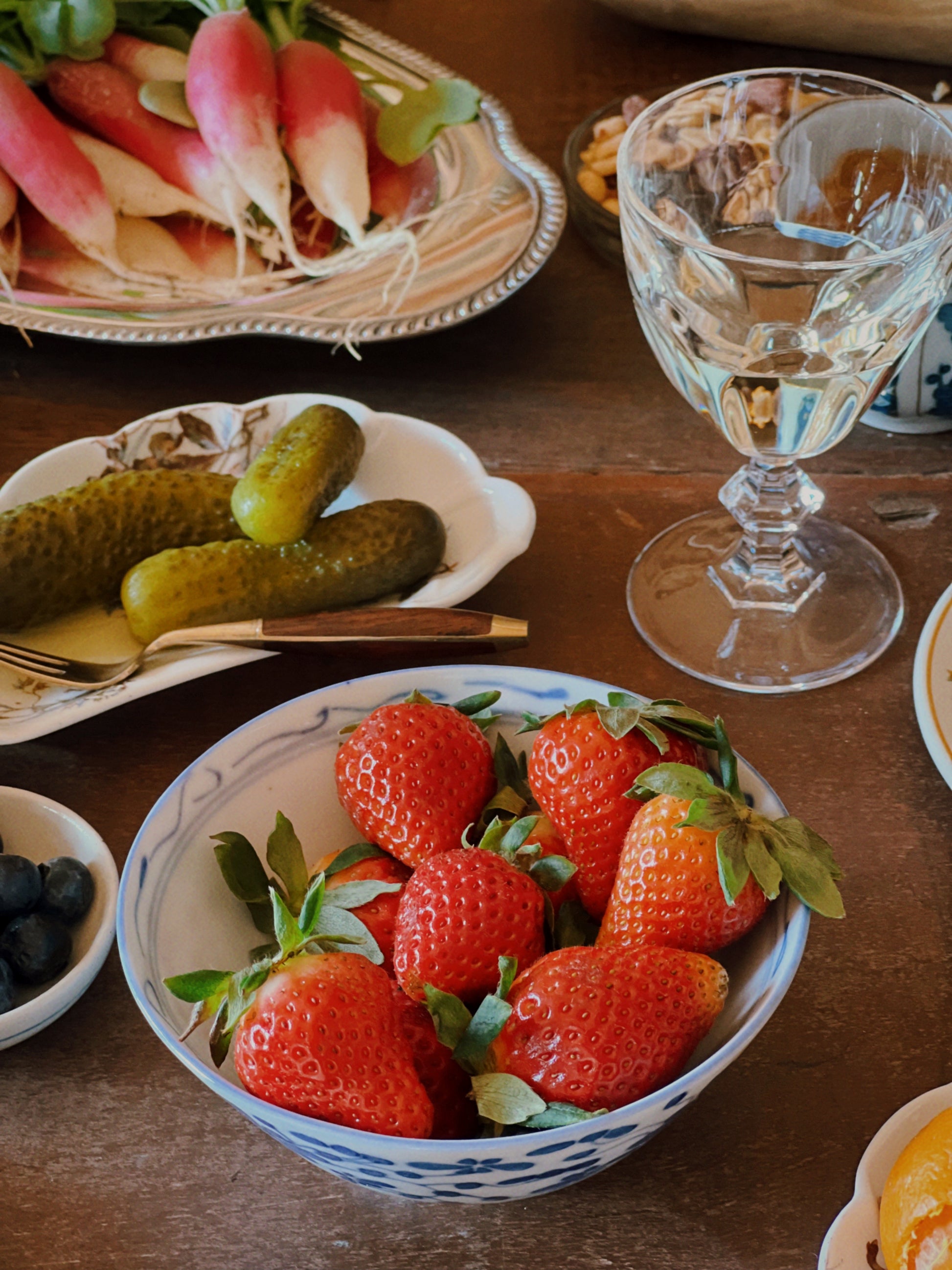 vintage blue and white floral rice bowl filled with strawberries on a rustic table with layered vintage tableware