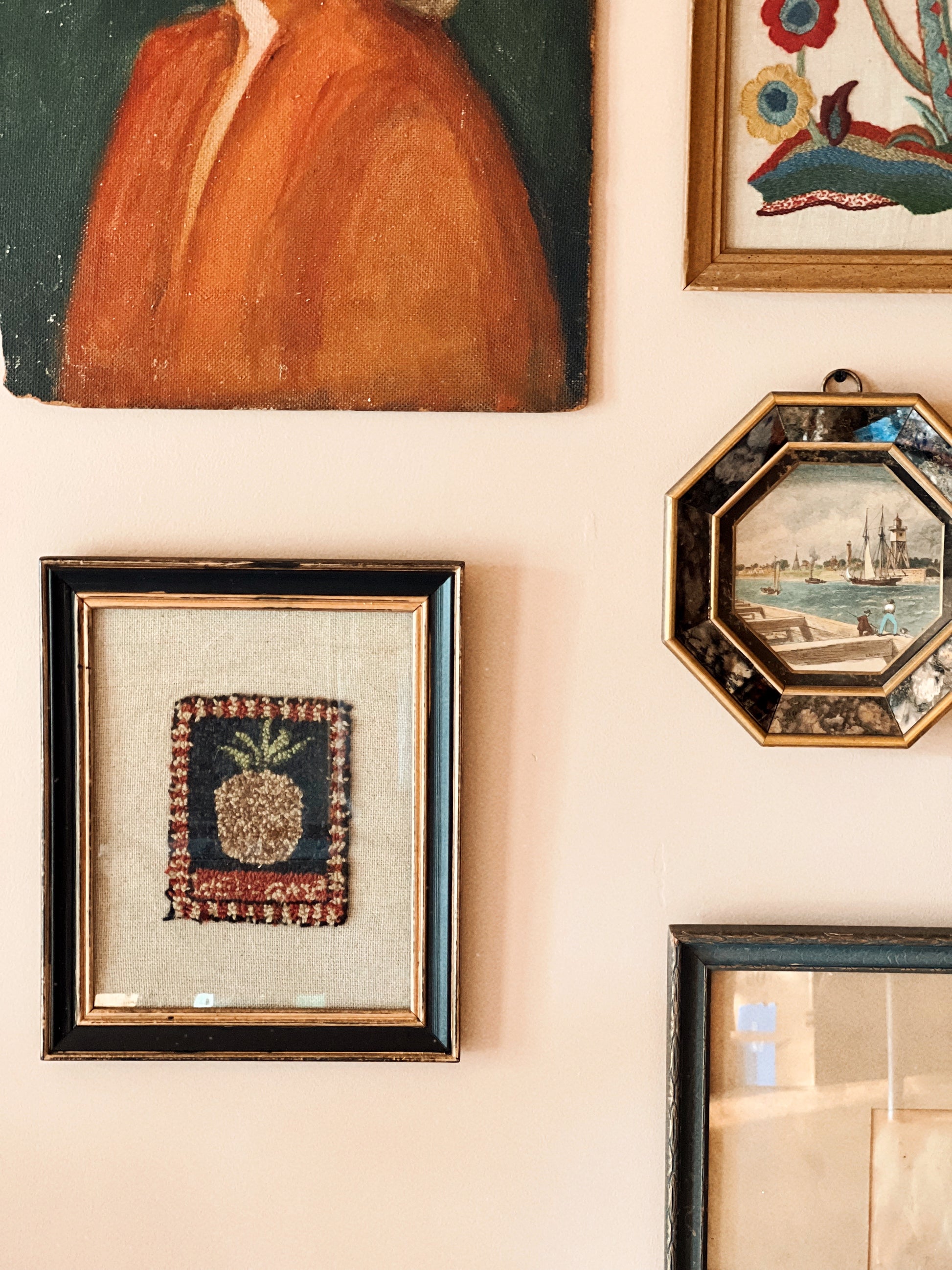 Framed vintage punch needle pineapple embroidery on linen, styled in an eclectic gallery wall with antique paintings and coastal artwork