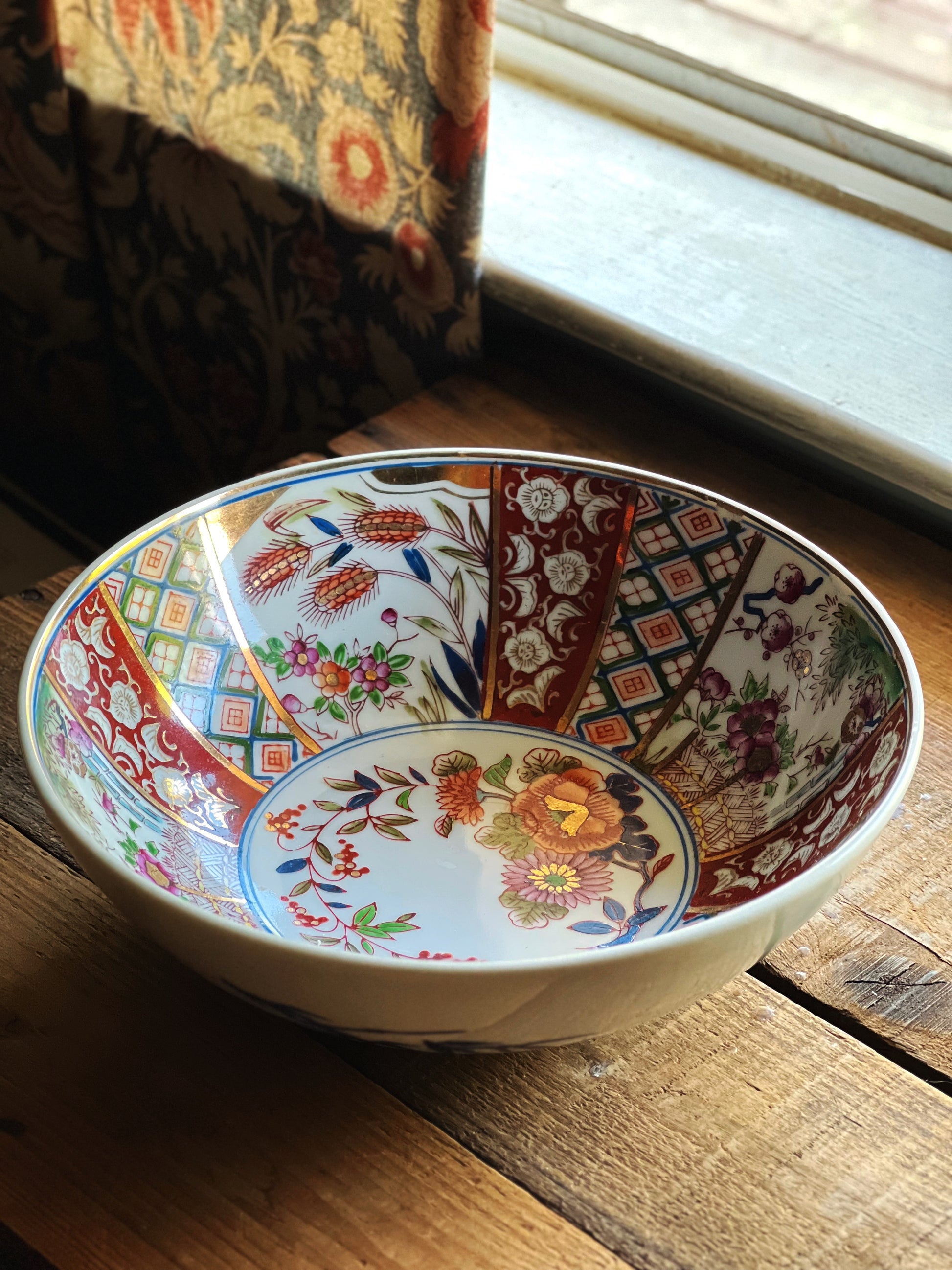 Vintage Japanese Imari style bowl with hand painted red blue and floral pattern styled on rustic wood table in natural light