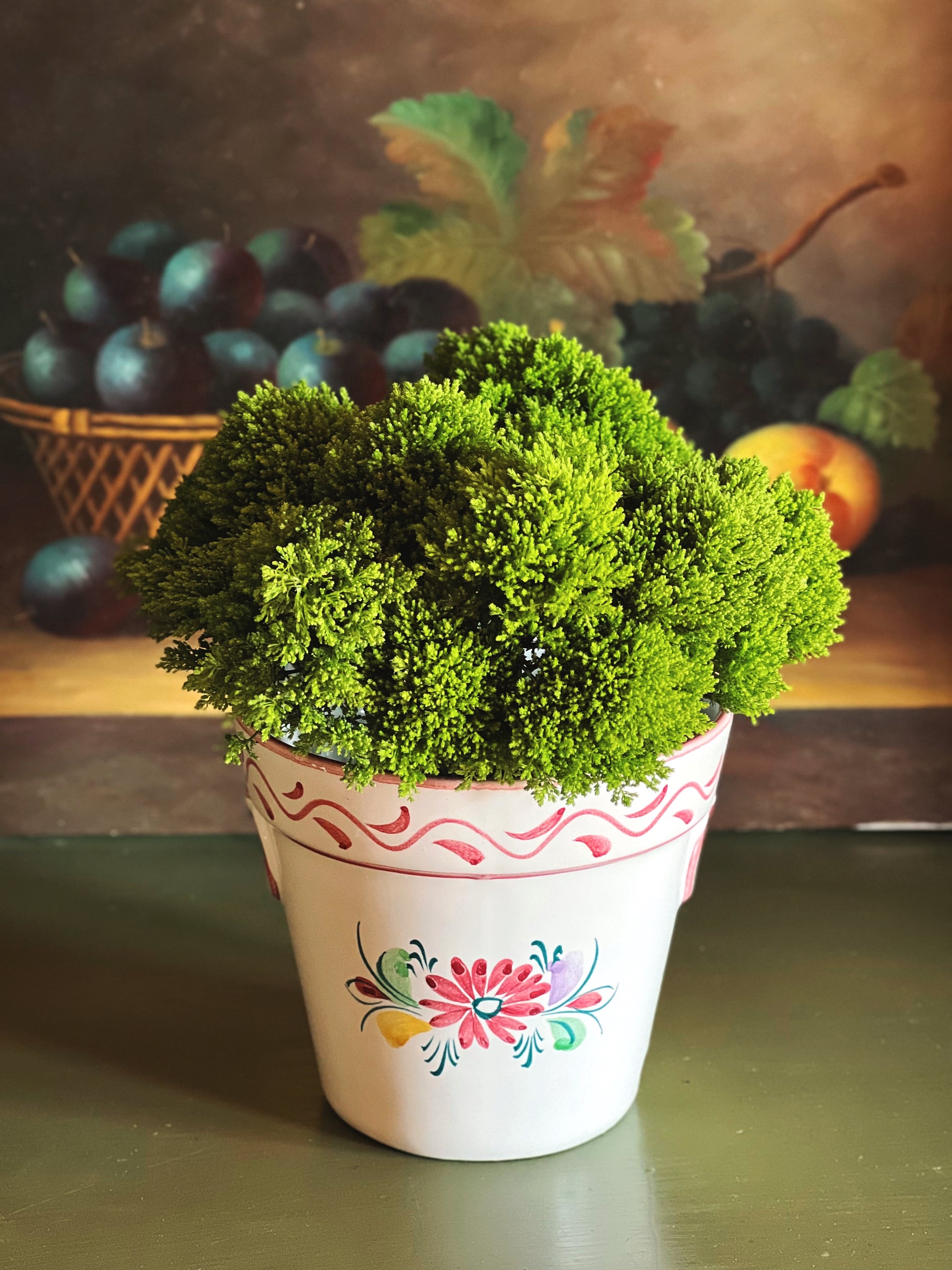 Hand painted vintage floral cache pot with green plant styled on table with fruit still life background