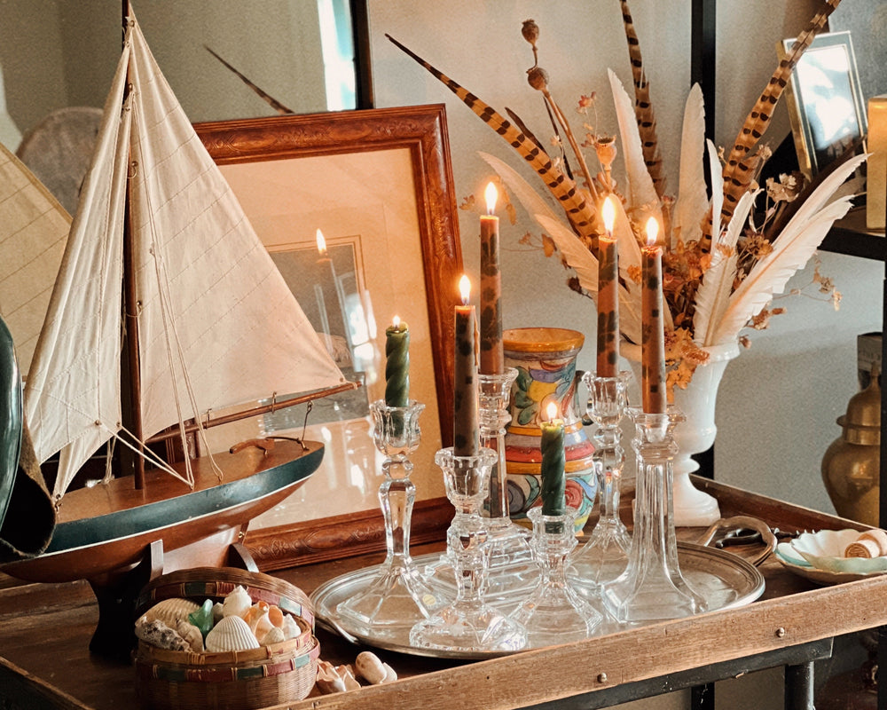 collected vintage candlesticks with lit tapers on pewter tray, styled with sailboat, shells, and framed art in a coastal interior