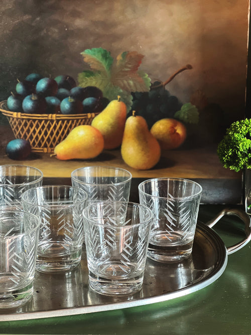 Vintage etched cocktail glasses arranged on a silver tray with pears and dark grapes in the background.