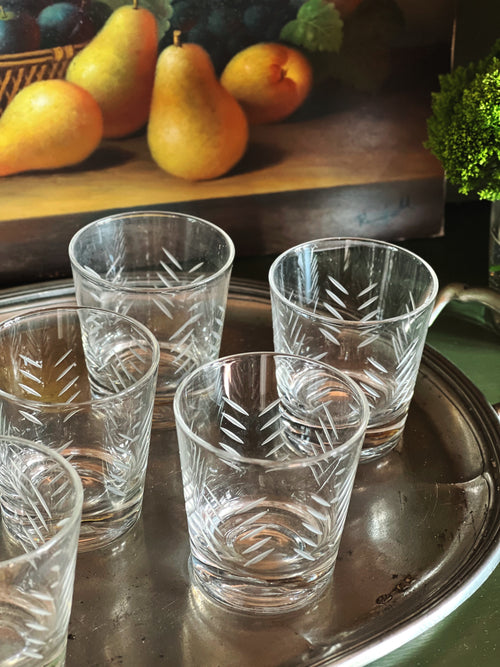 Overhead angle of vintage etched cocktail glasses arranged on a silver tray with pears and dark grapes in the background.