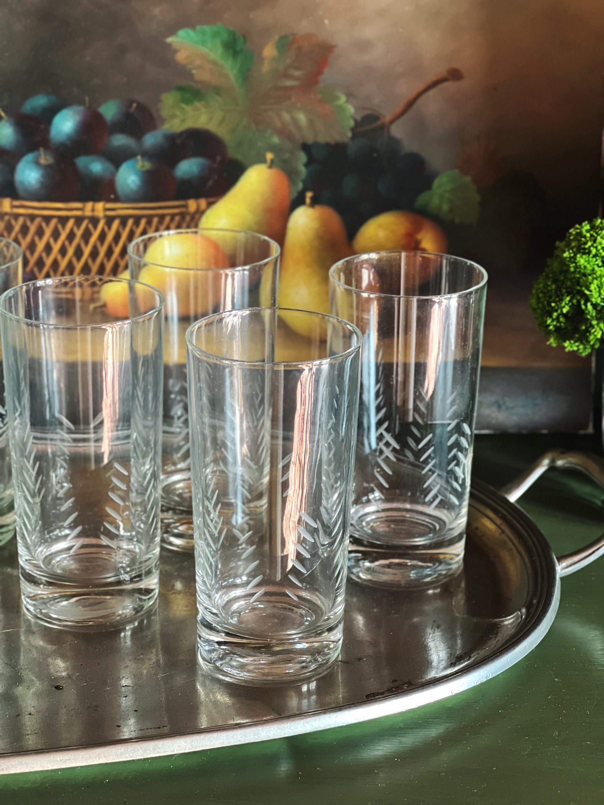 Vintage etched highball glasses displayed on a silver tray with pears and dark grapes in the background.