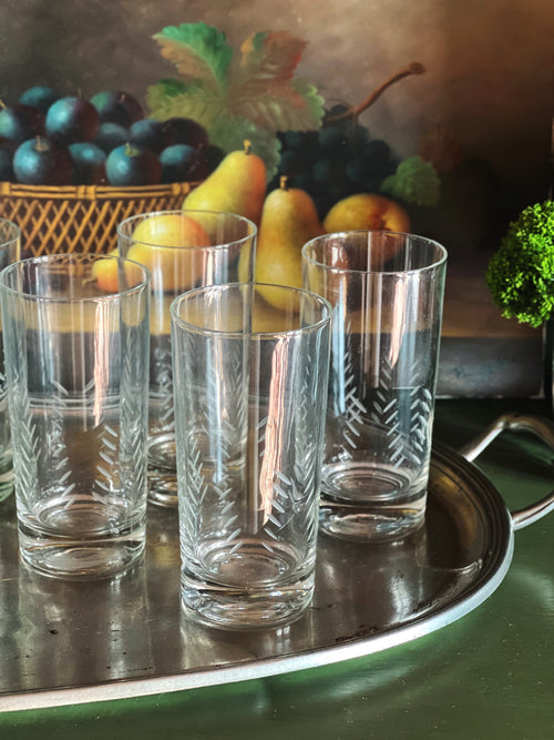 Vintage etched highball glasses displayed on a silver tray with pears and dark grapes in the background.