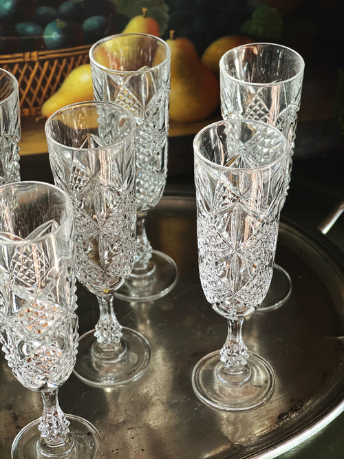 Overhead angle of a set of crystal glasses on a reflective surface with a fruit basket in the background