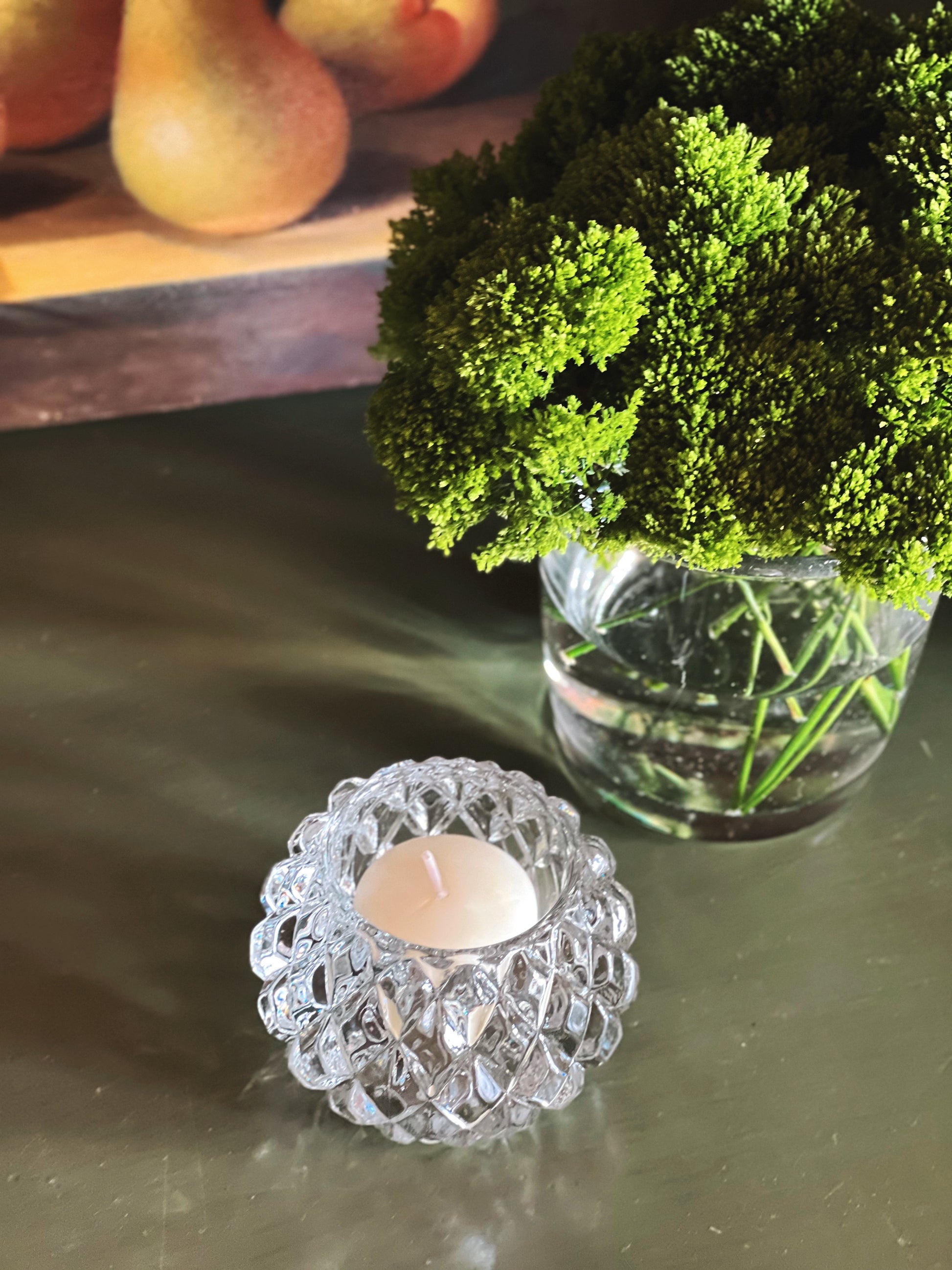 overhead view of a bubble glass votive holder next to a vase of greenery