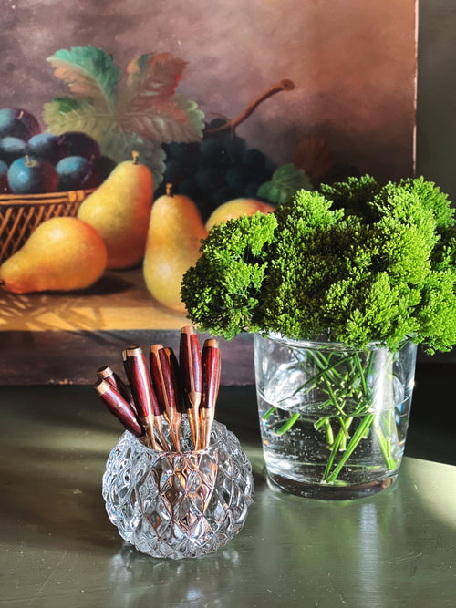 glass votive holder holding demitasse spoons next to a floral arrangement