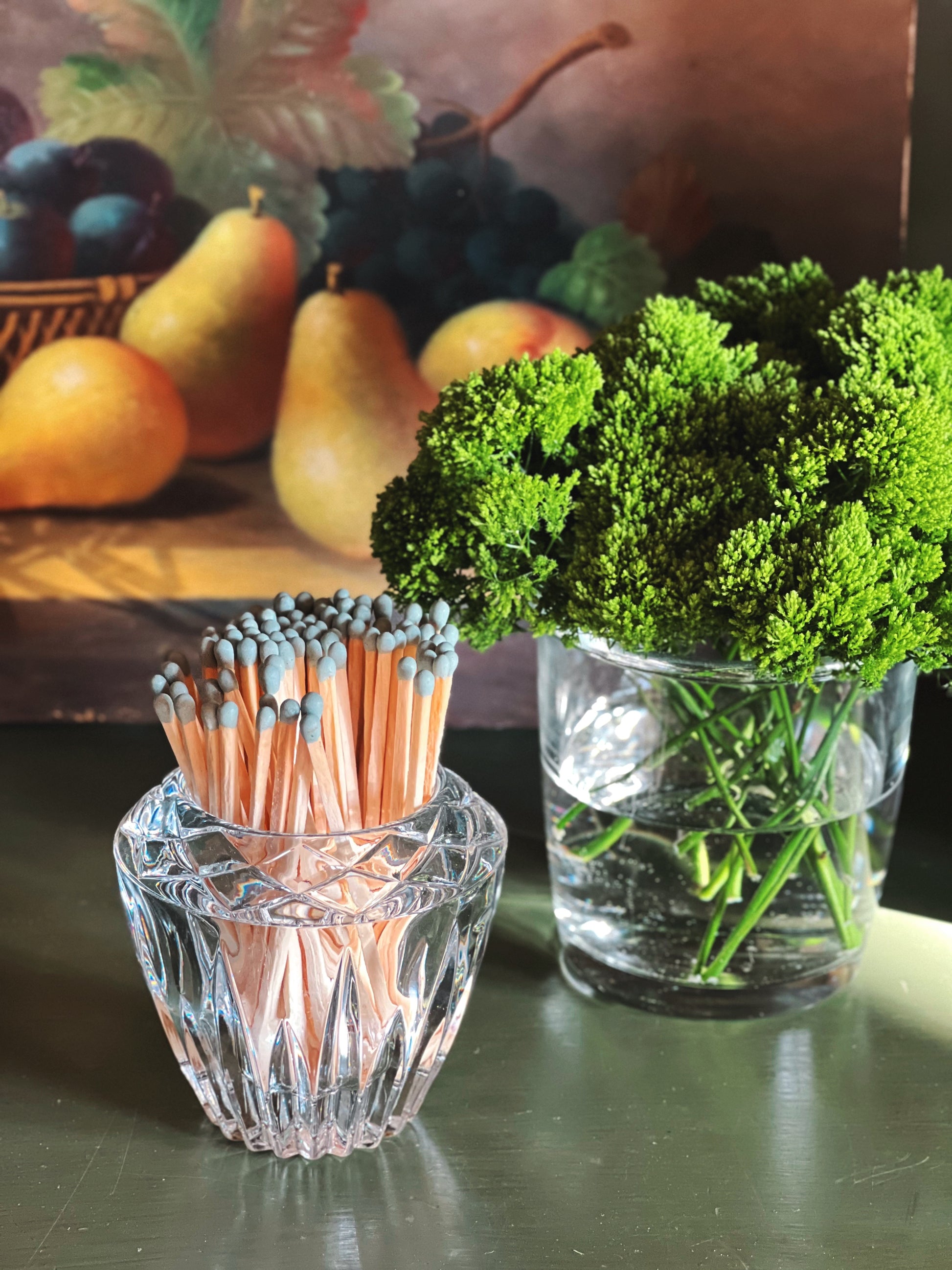 Tall vintage crystal votive holder styled with matches beside greenery and fruit for gathered entertaining decor