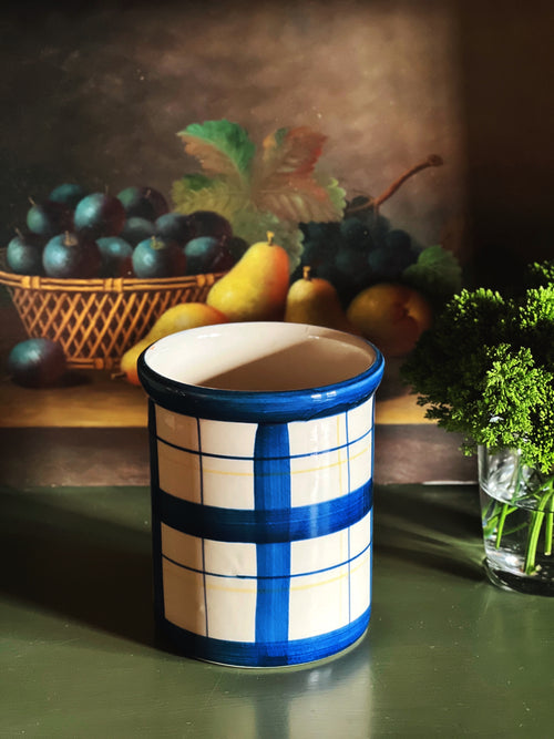 Vintage blue plaid ceramic crock styled on green surface with fruit and moody still life background