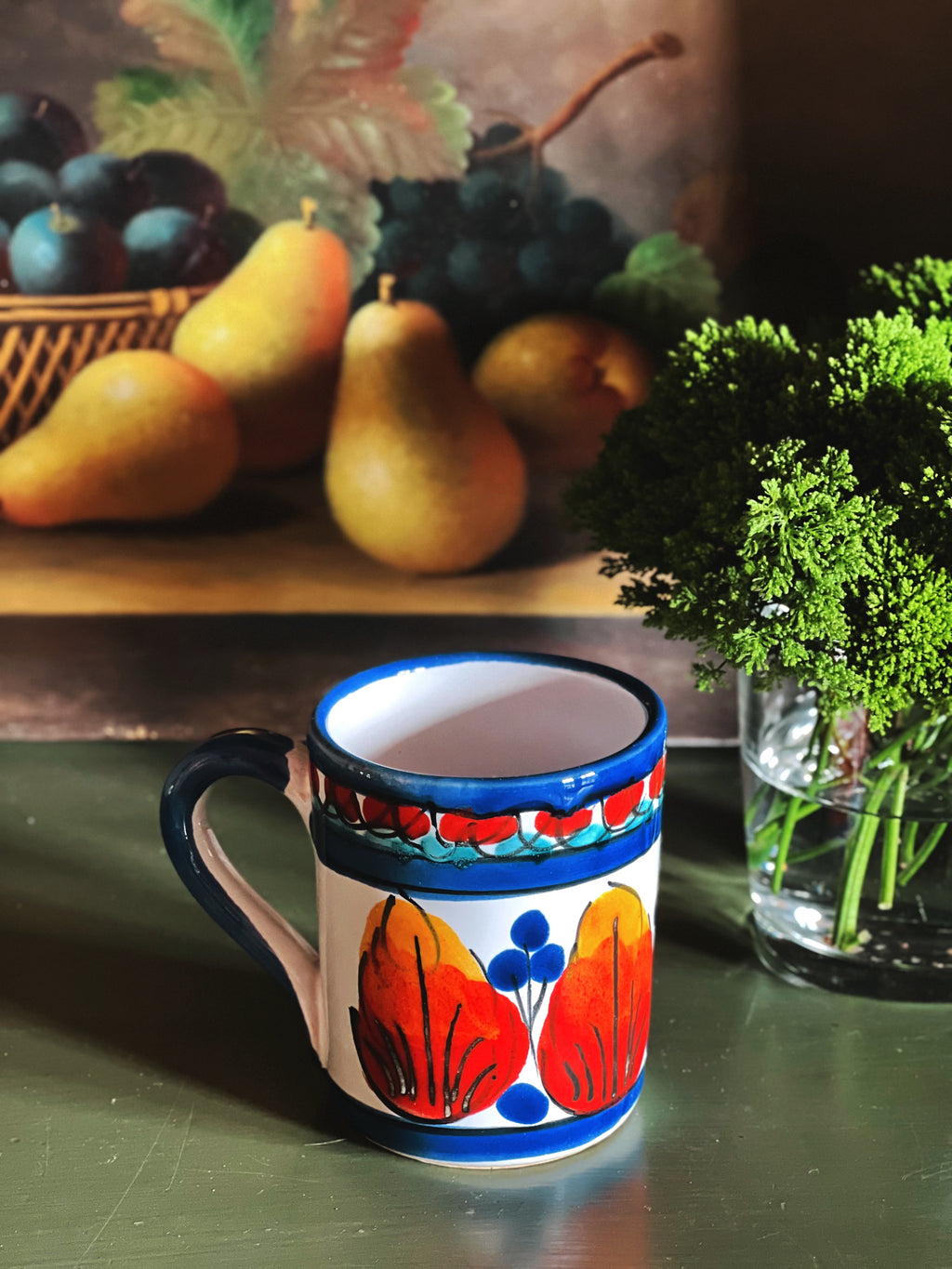 Hand painted vintage ceramic mug with colorful folk design styled with fruit on green surface