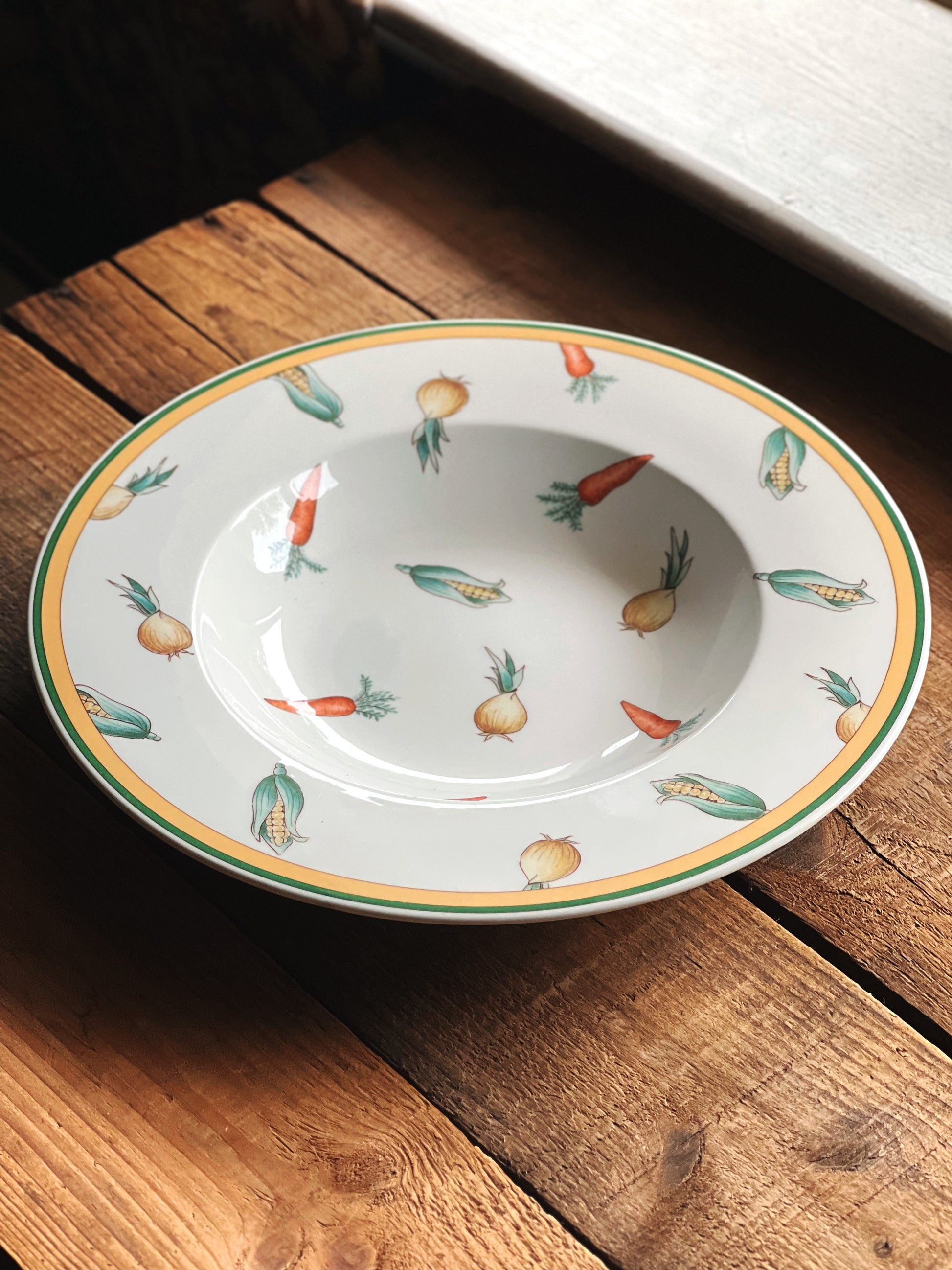 Angled side view of a Villeroy & Boch A La Ferme rimmed soup bowl on a rustic wood surface